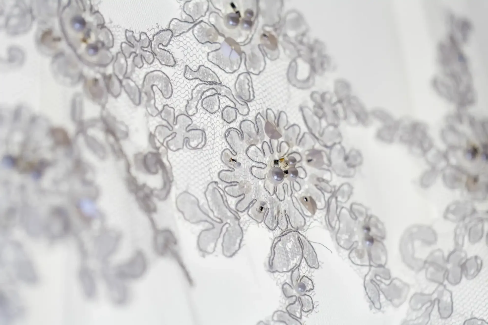Close-up of a white lace fabric with intricate floral embroidery and small bead embellishments.
