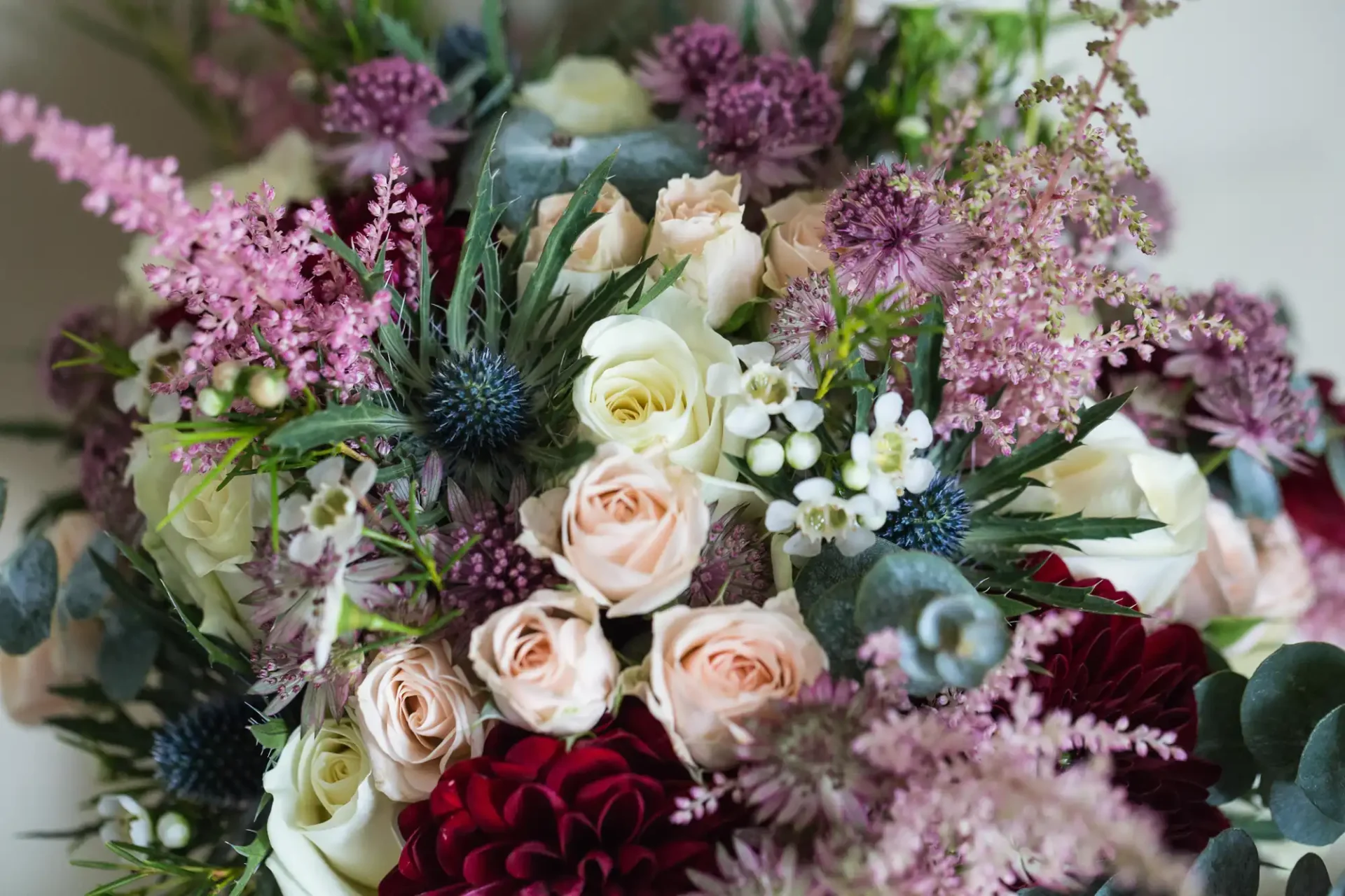 Close-up of a floral arrangement featuring pale pink roses, deep red dahlias, purple asters, white blooms, and green foliage.