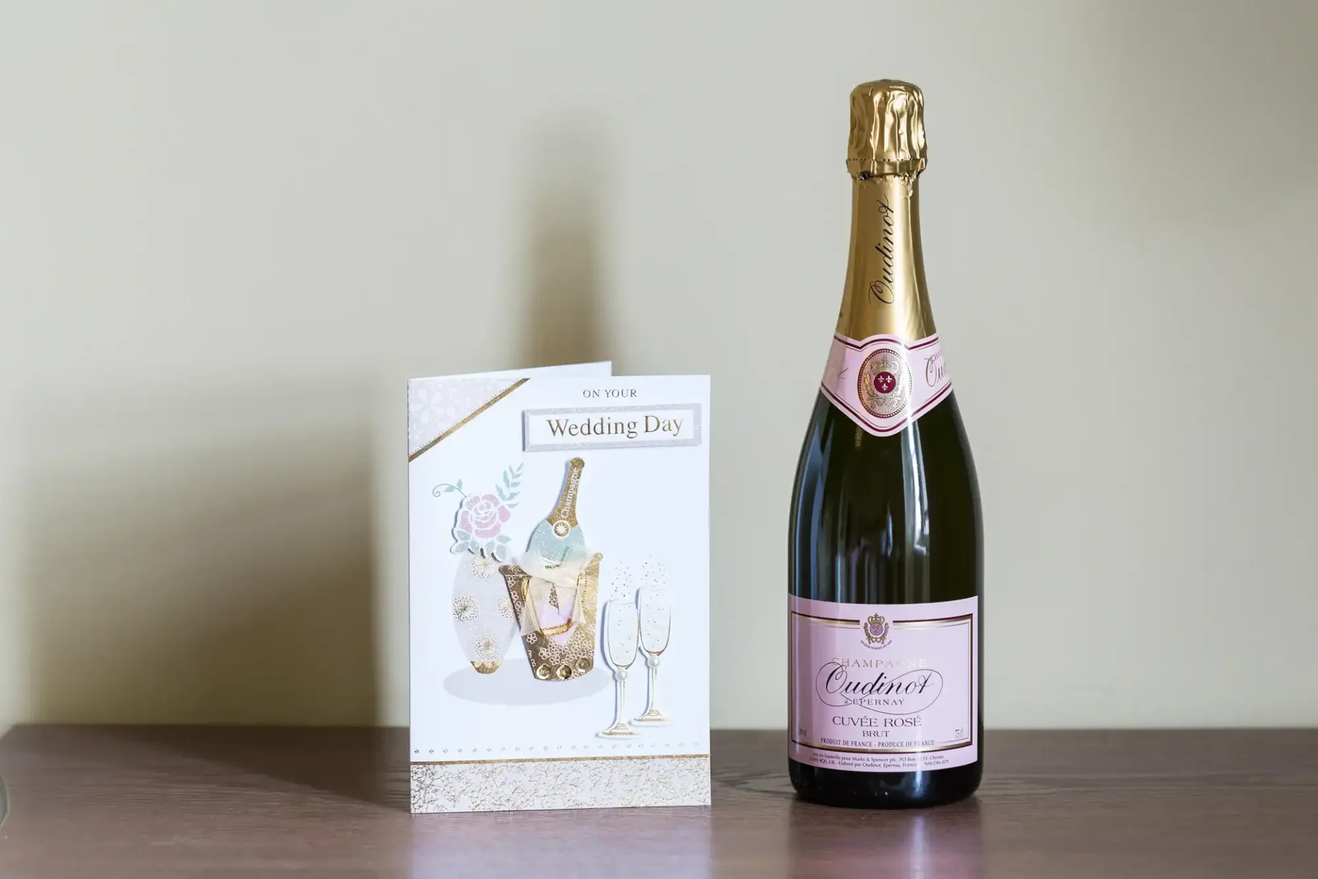 A wedding day card and a bottle of cuvée rosé champagne on a table.