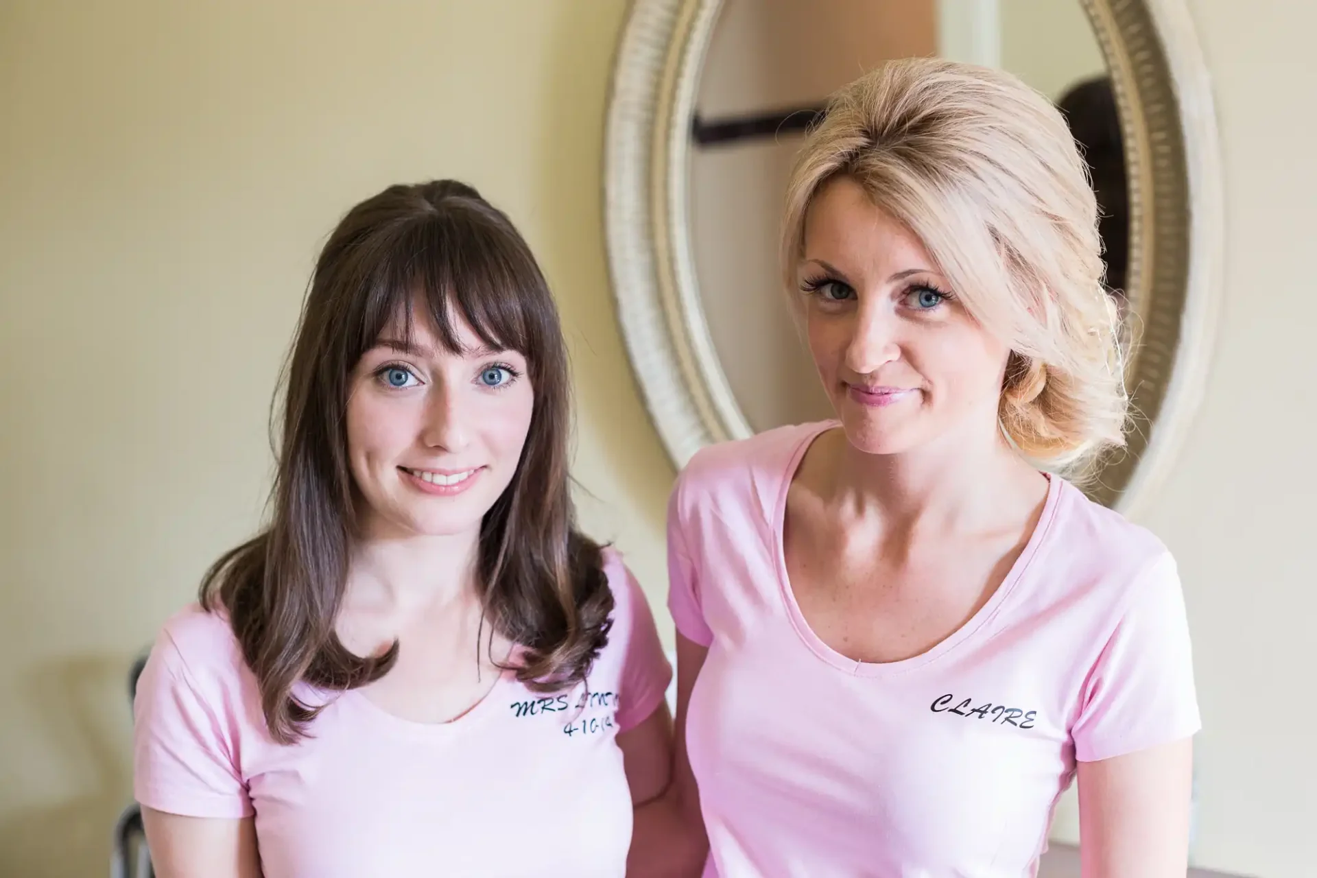 Two women wearing pink t-shirts with name tags, "nicola" and "claire," smiling and seated in front of a mirror.