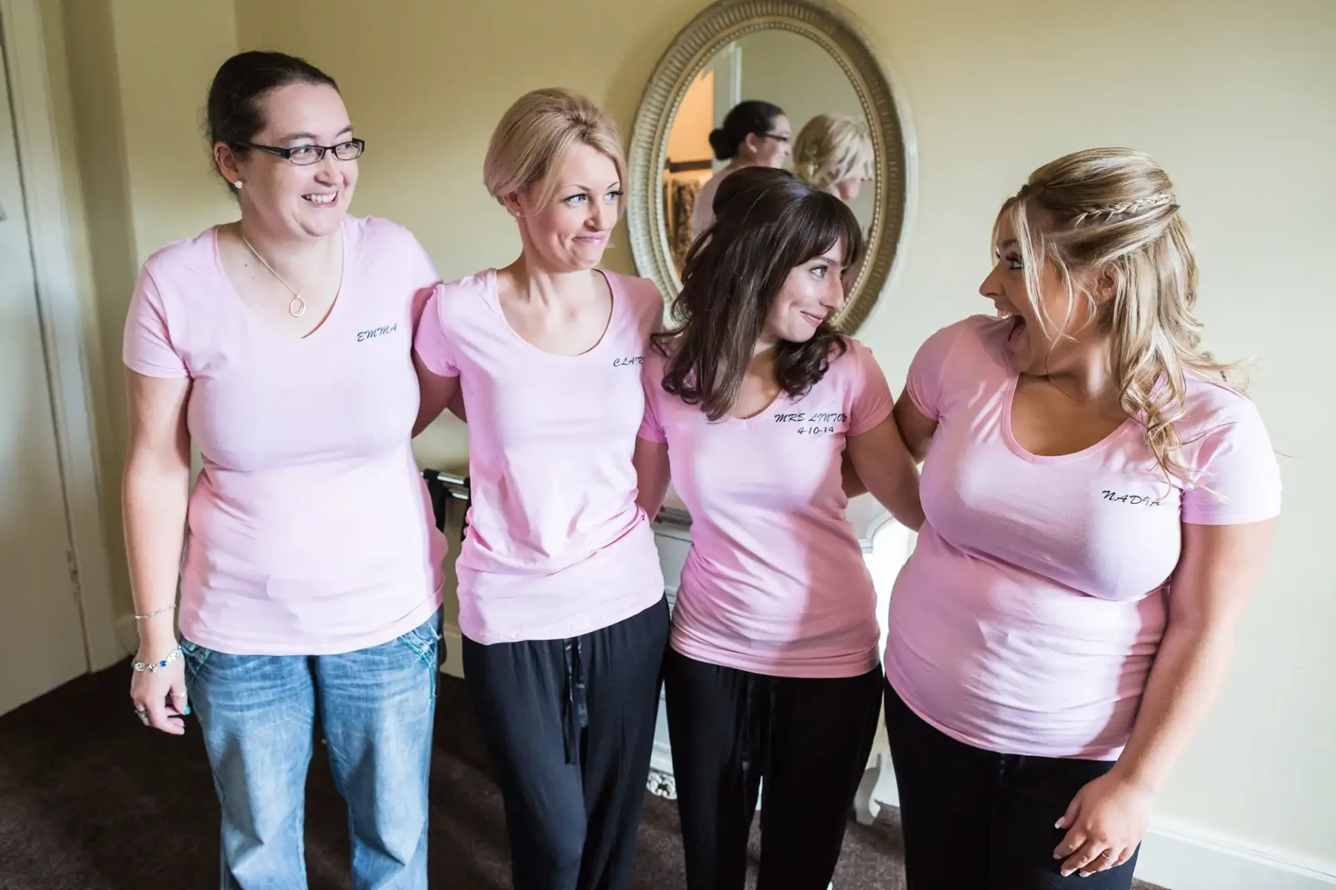 Four women in matching pink t-shirts smiling and interacting in a room, with names on their shirts: jessica, cathy, beth, and taylor.