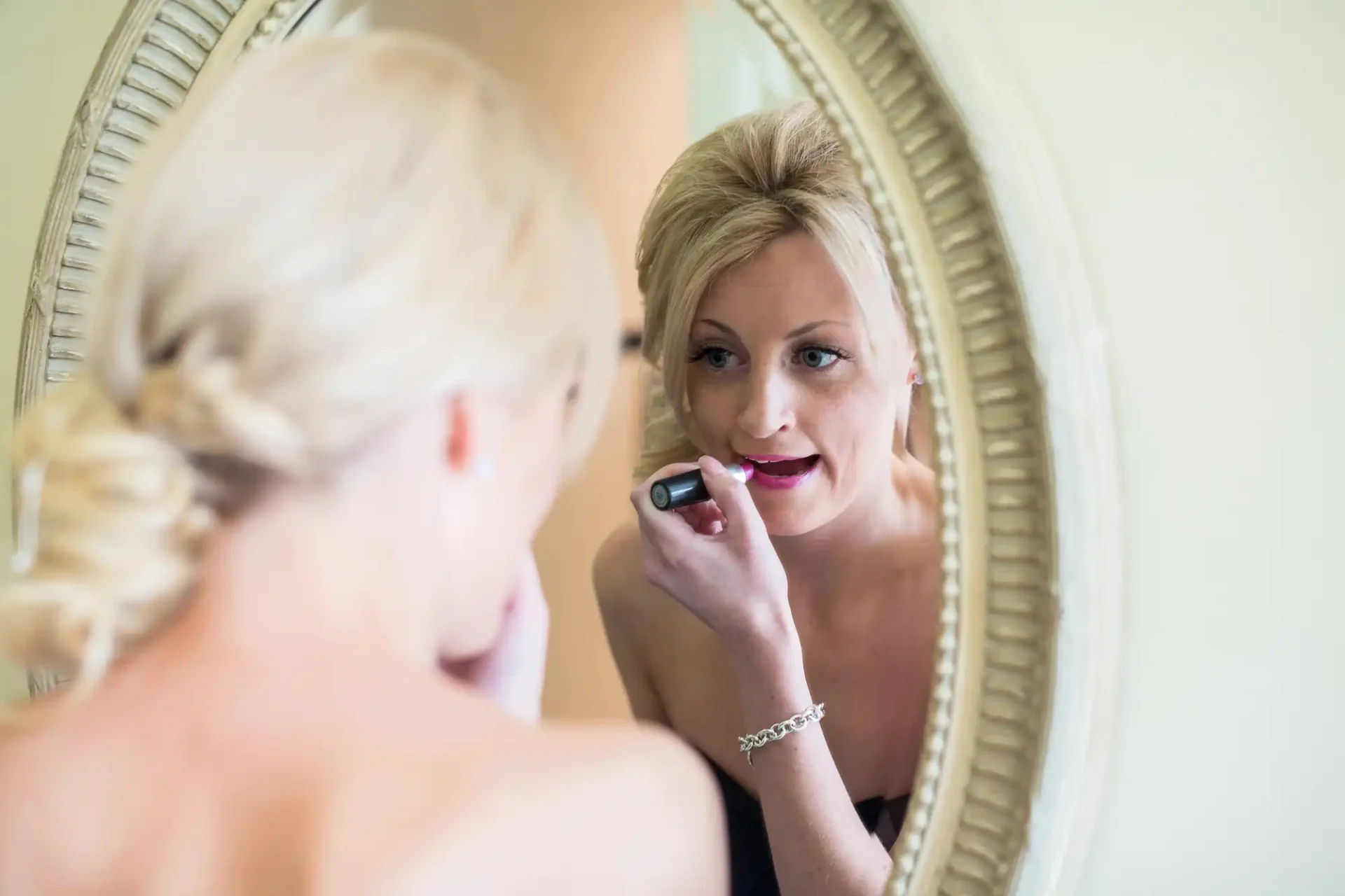 A woman applying lipstick while looking at her reflection in a mirror.