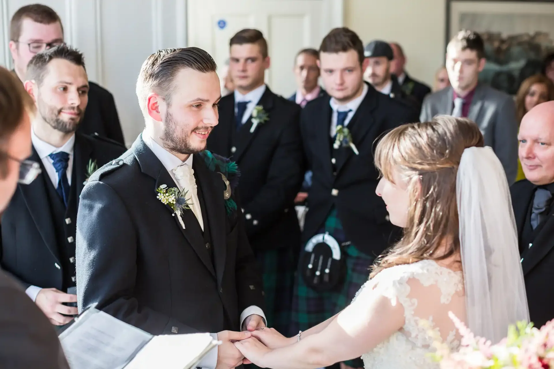 Bride and groom holding hands at their wedding ceremony, surrounded by guests, with one groomsmen wearing a kilt.