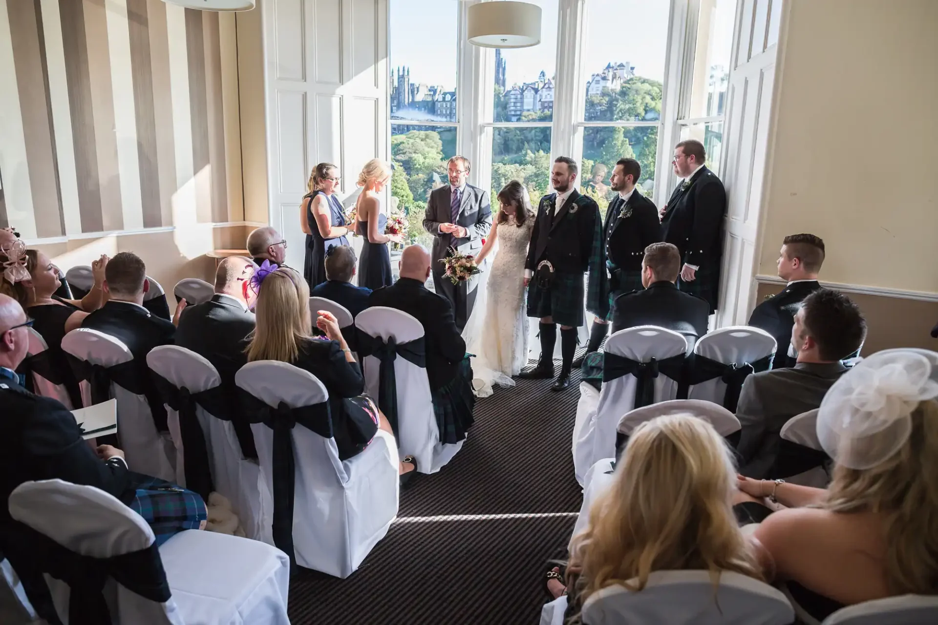A wedding ceremony indoors with guests seated on both sides watching as the bride and groom stand at the altar, surrounded by the wedding party.