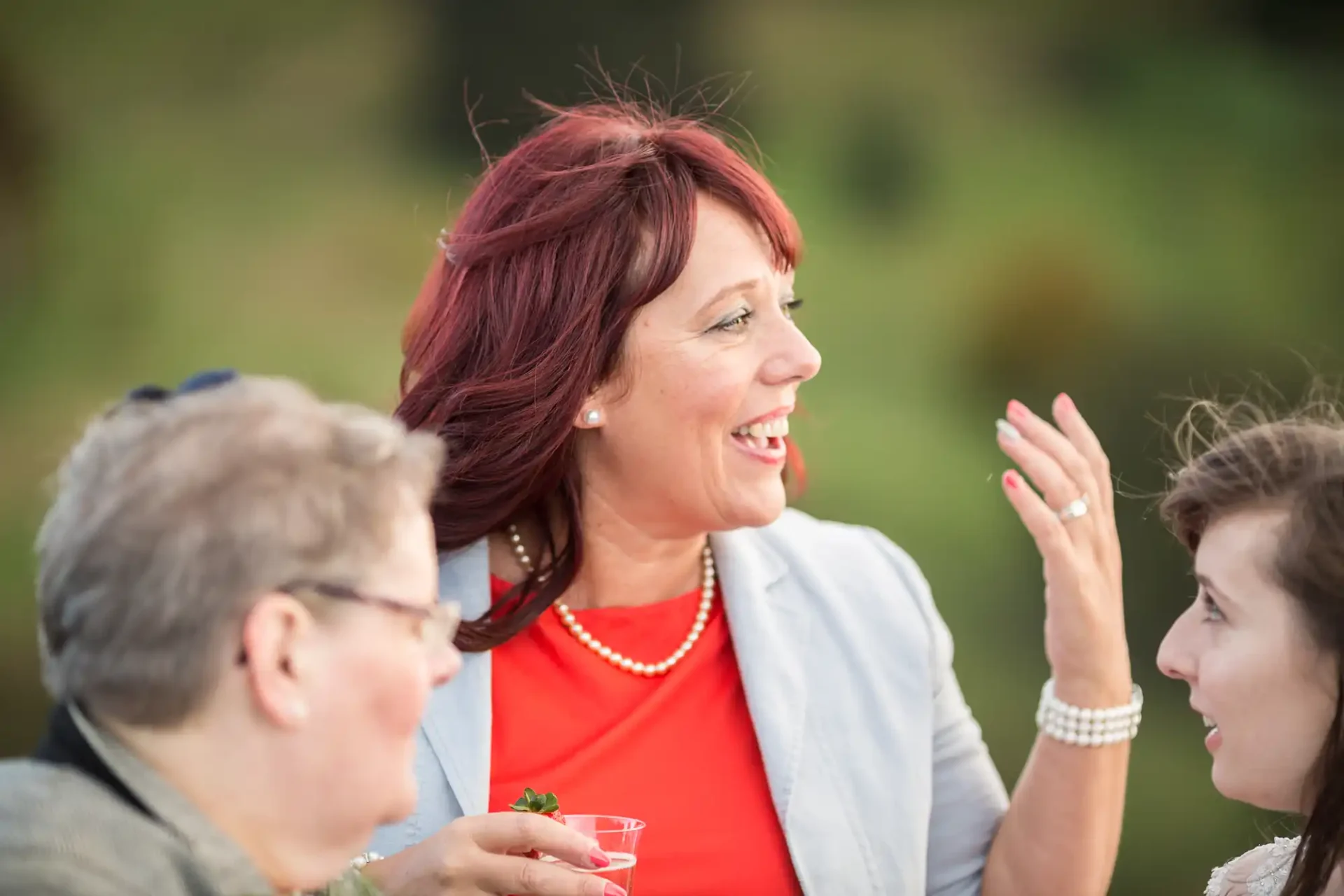 A woman with red hair laughing and talking with two people at an outdoor gathering.