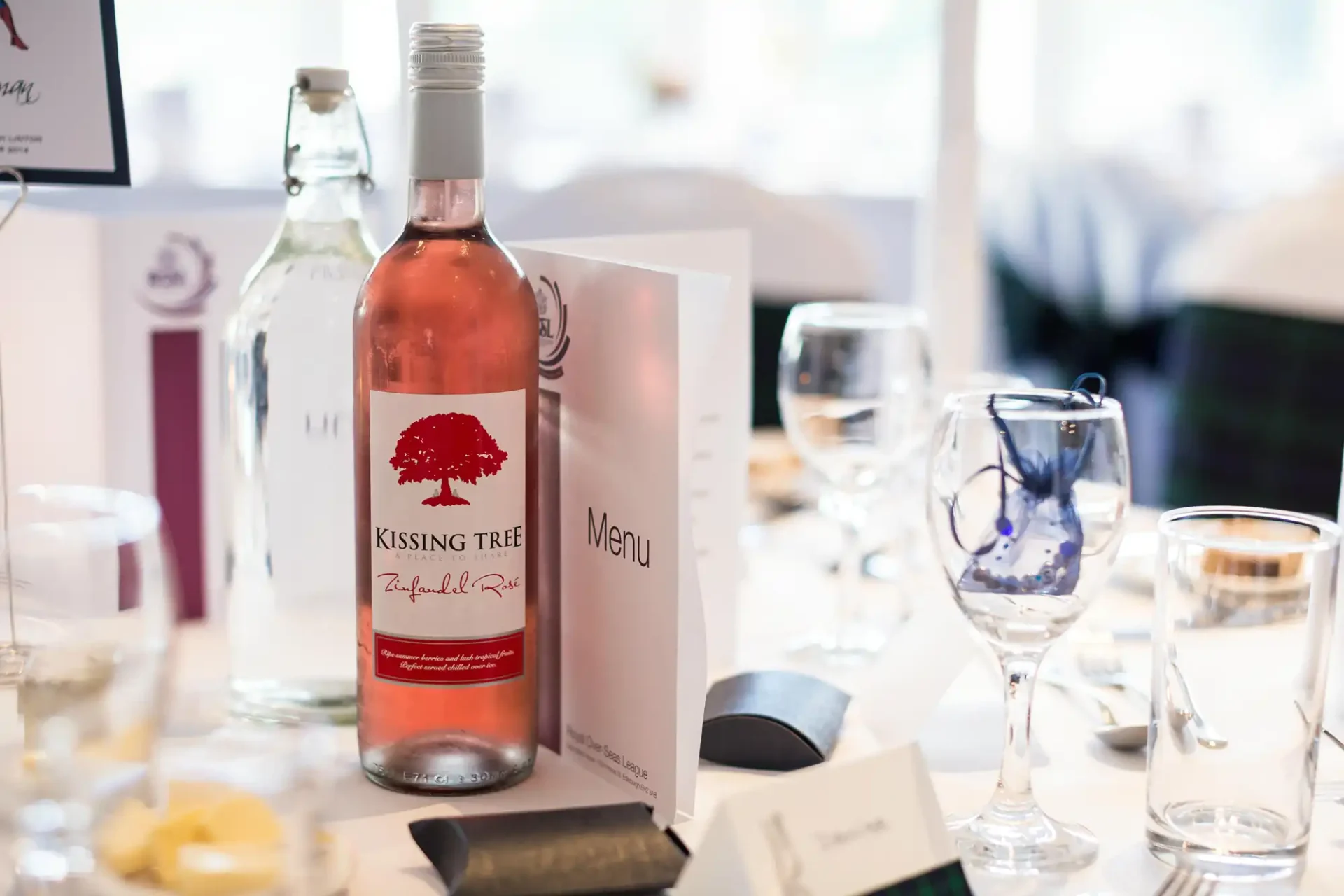 A bottle of kissing tree rosé wine positioned on a decorated dining table with menus and glasses.