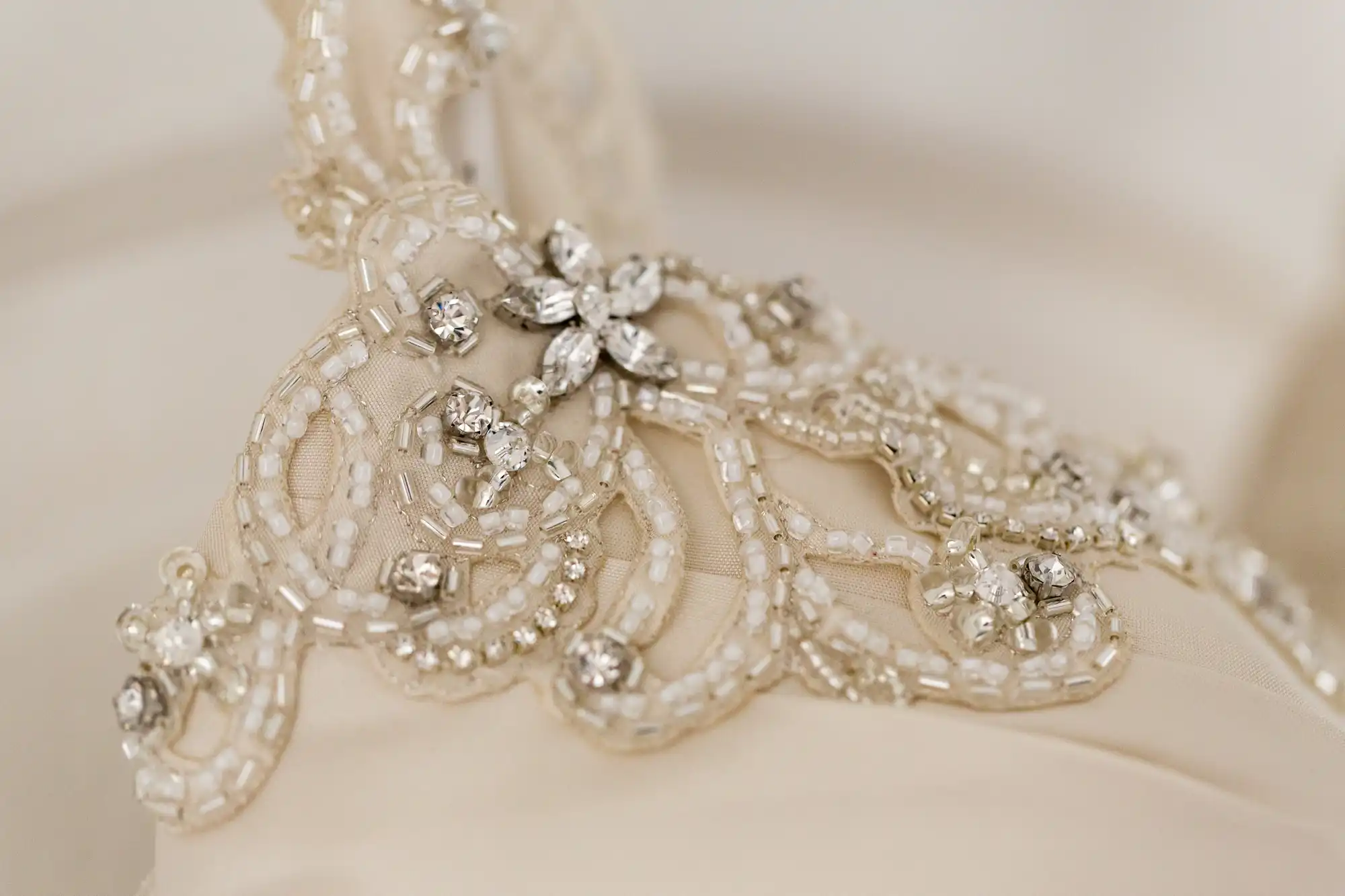 Close-up of an intricate bridal headpiece with delicate beadwork and crystal embellishments on a beige fabric.