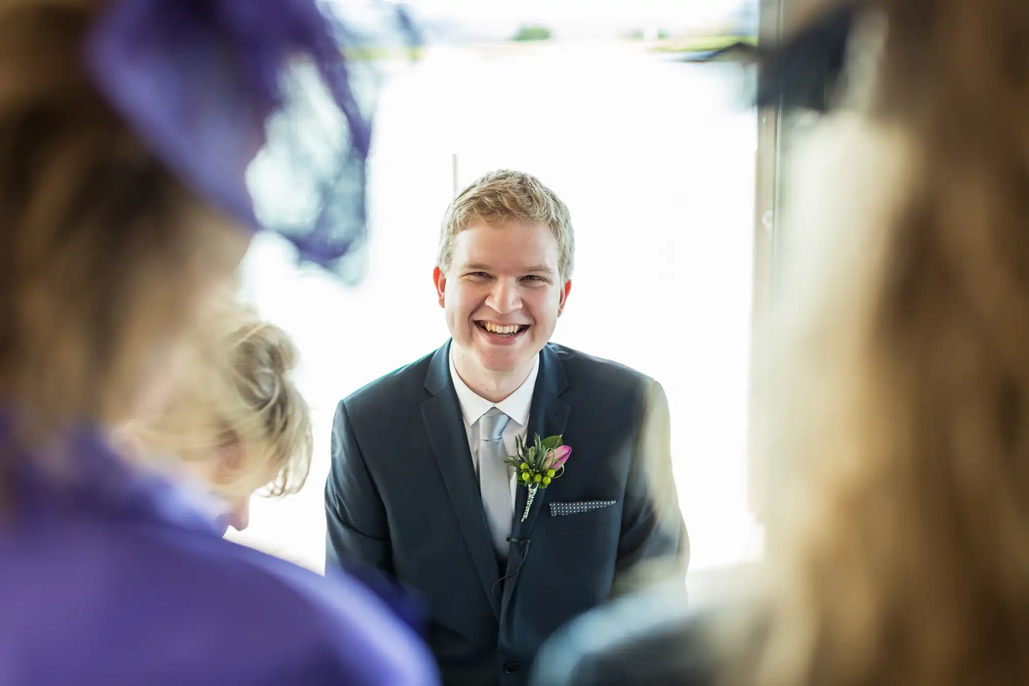 Groom smiling joyously, framed between guests at a wedding ceremony.