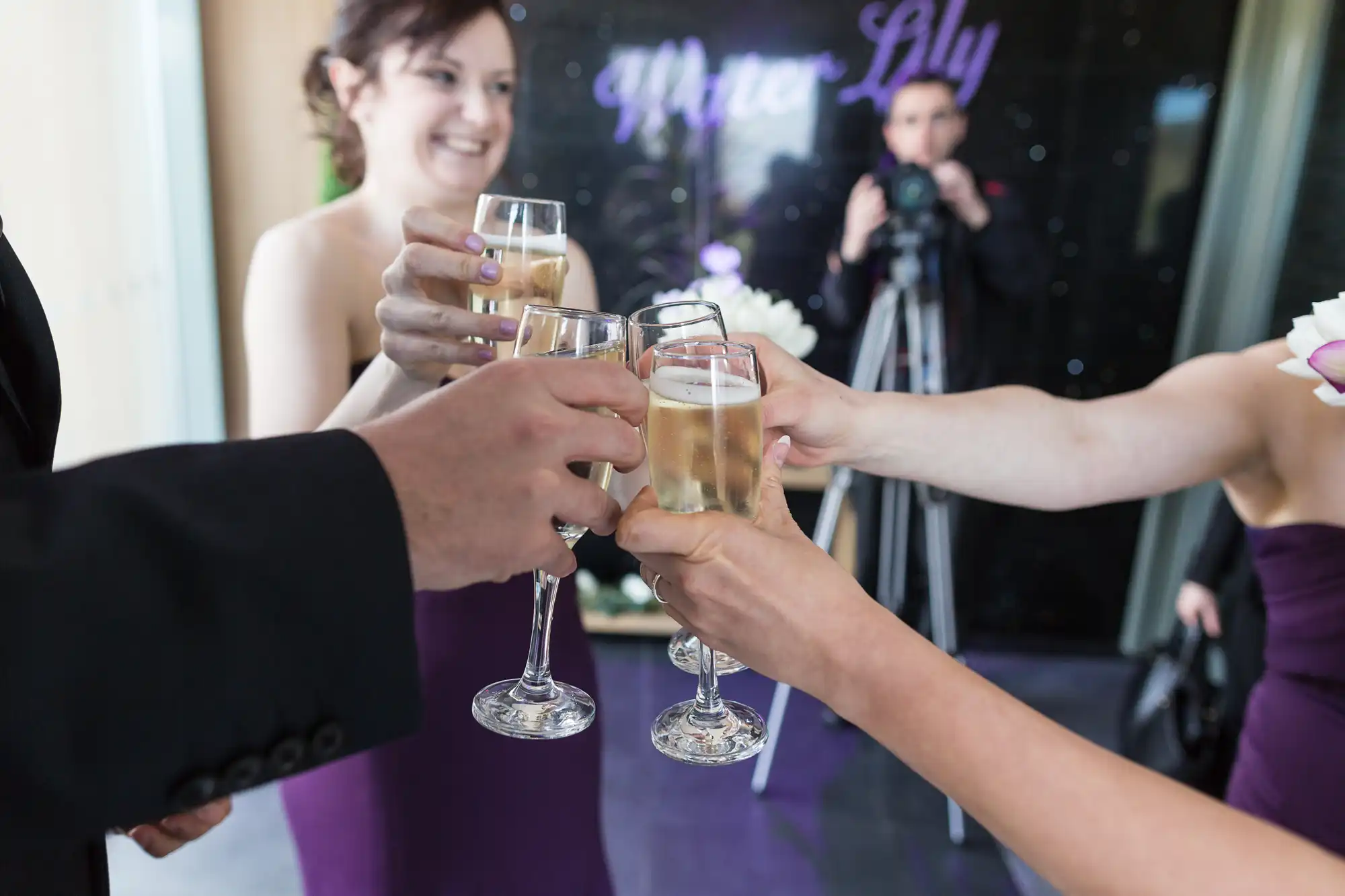 Group of people toasting with champagne glasses at a celebratory event, with a photographer in the background.