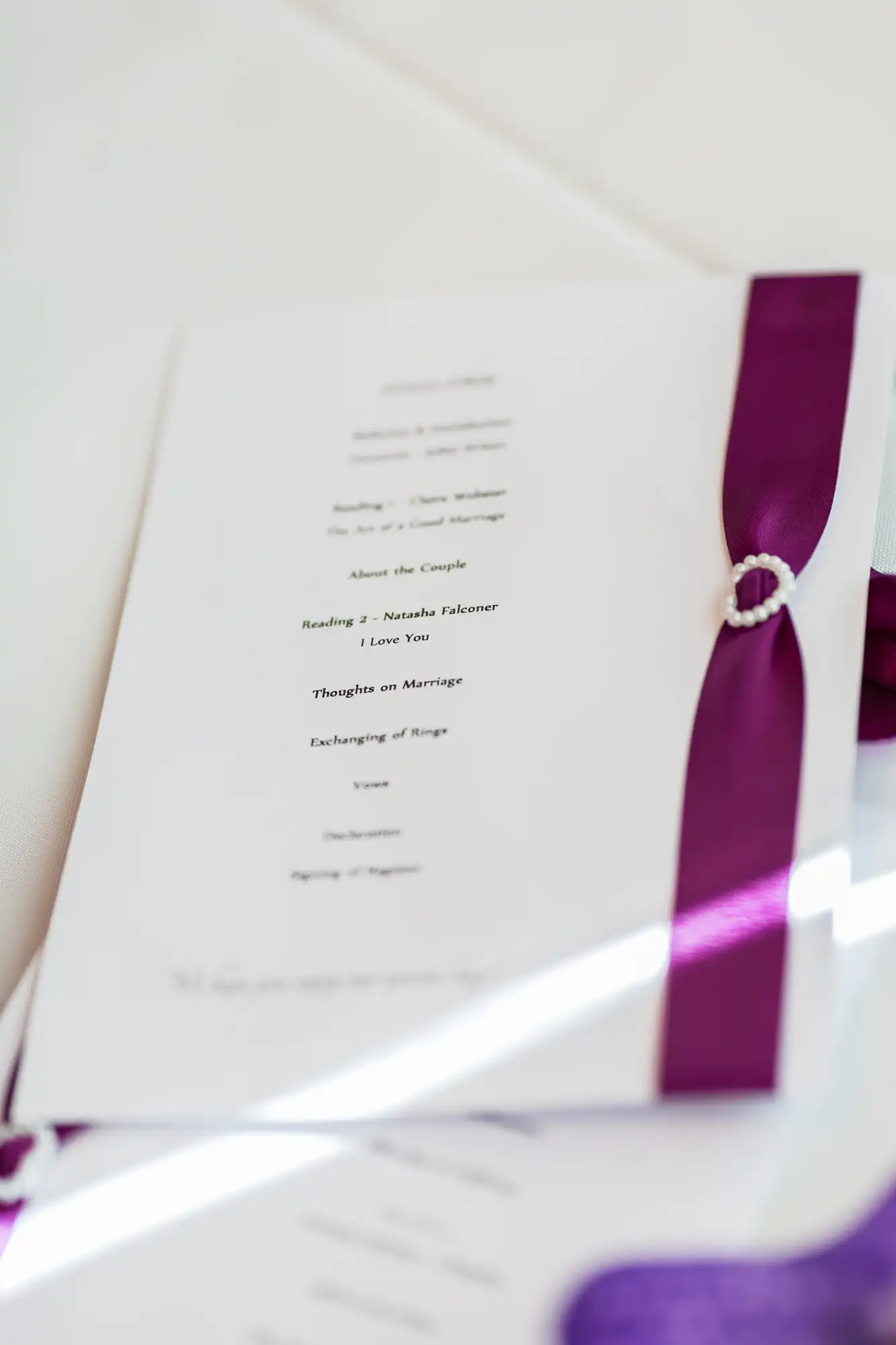 A close-up of a wedding program tied with a purple ribbon, featuring a section titled "thoughts on marriage.