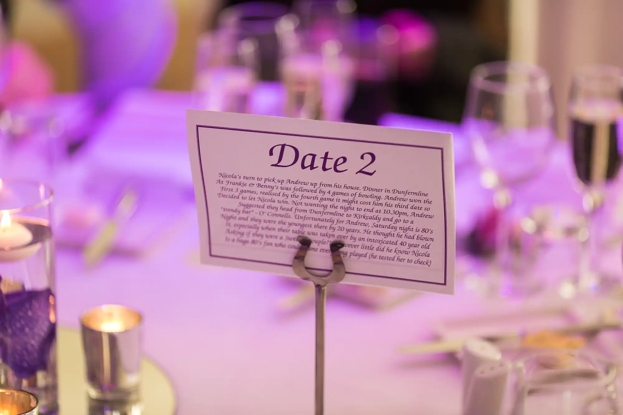 Table setting with a "date 2" placard, candles, and wine glasses at a dimly lit event.