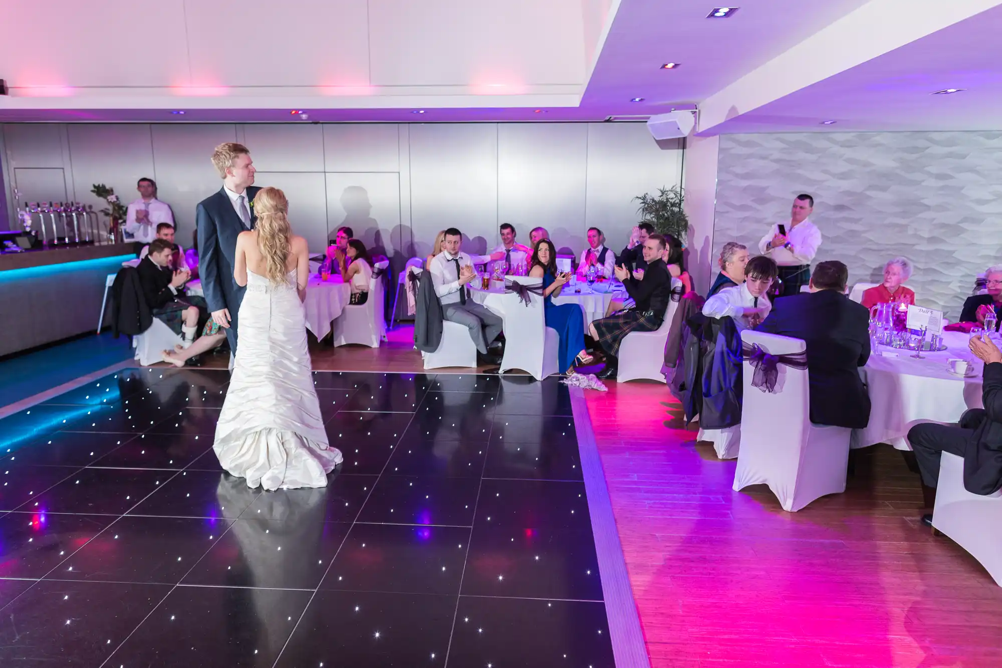 Bride and groom sharing their first dance at a wedding reception with guests seated around the dance floor.