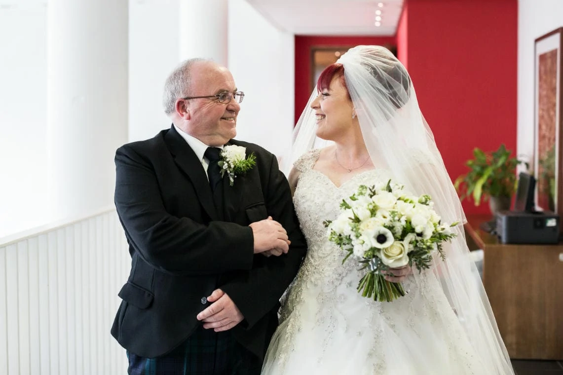 bride and her father smiling at each other as they make their way to the ceremony room