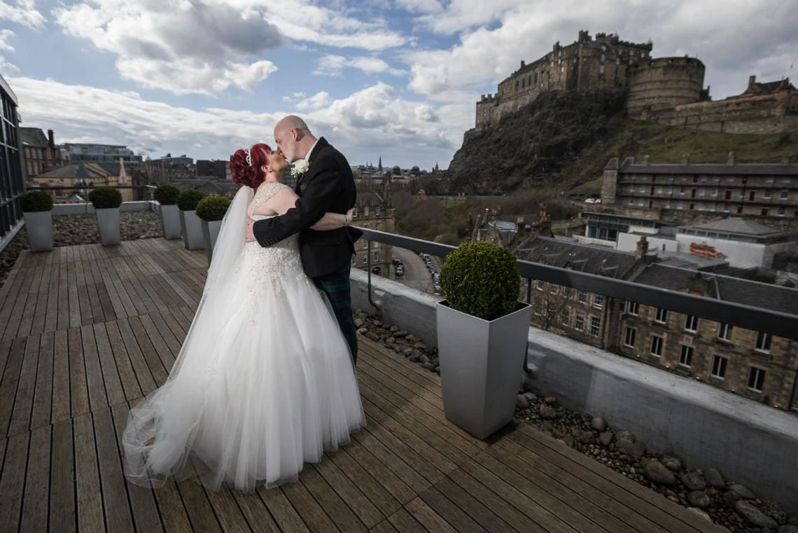 newlyweds kissing on the balcony outside Heights restaurant with Edinburgh Castle in the background