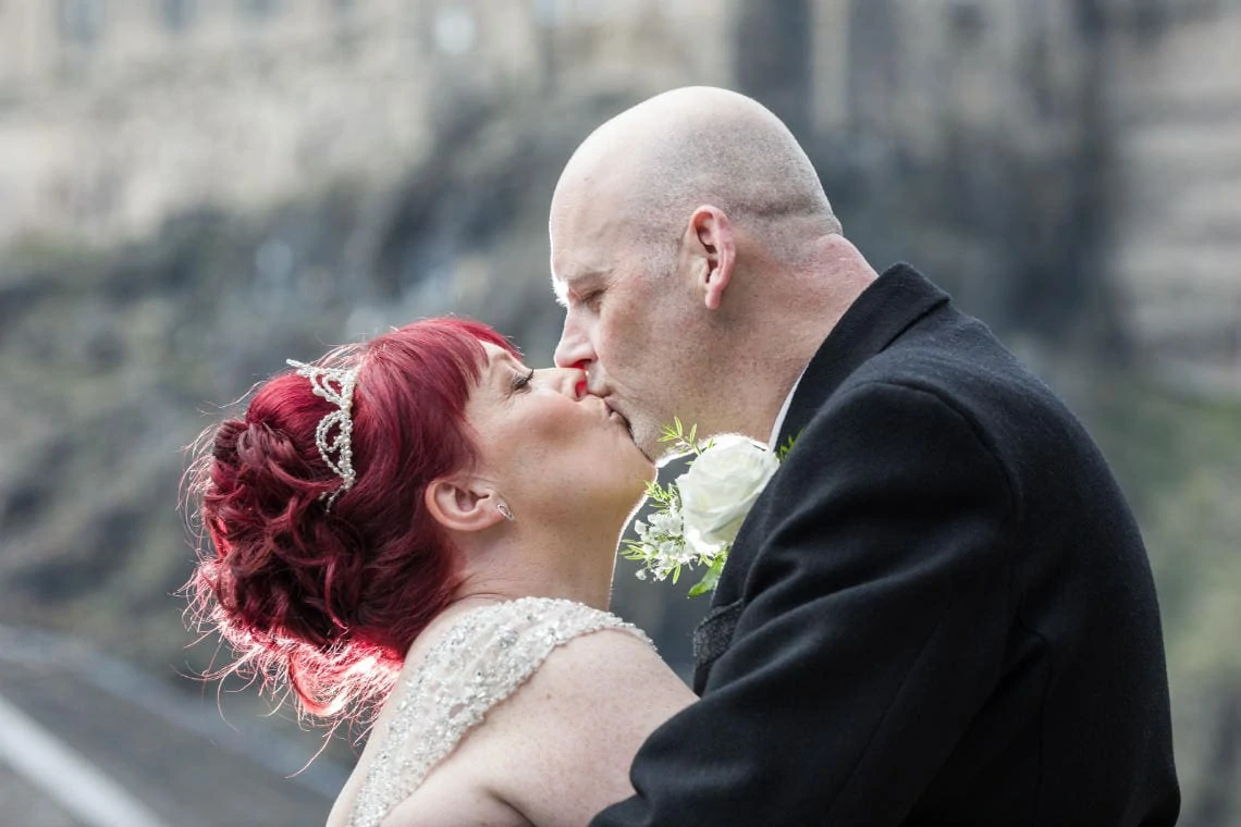 newlyweds kiss on balcony with Edinburgh Castle in background