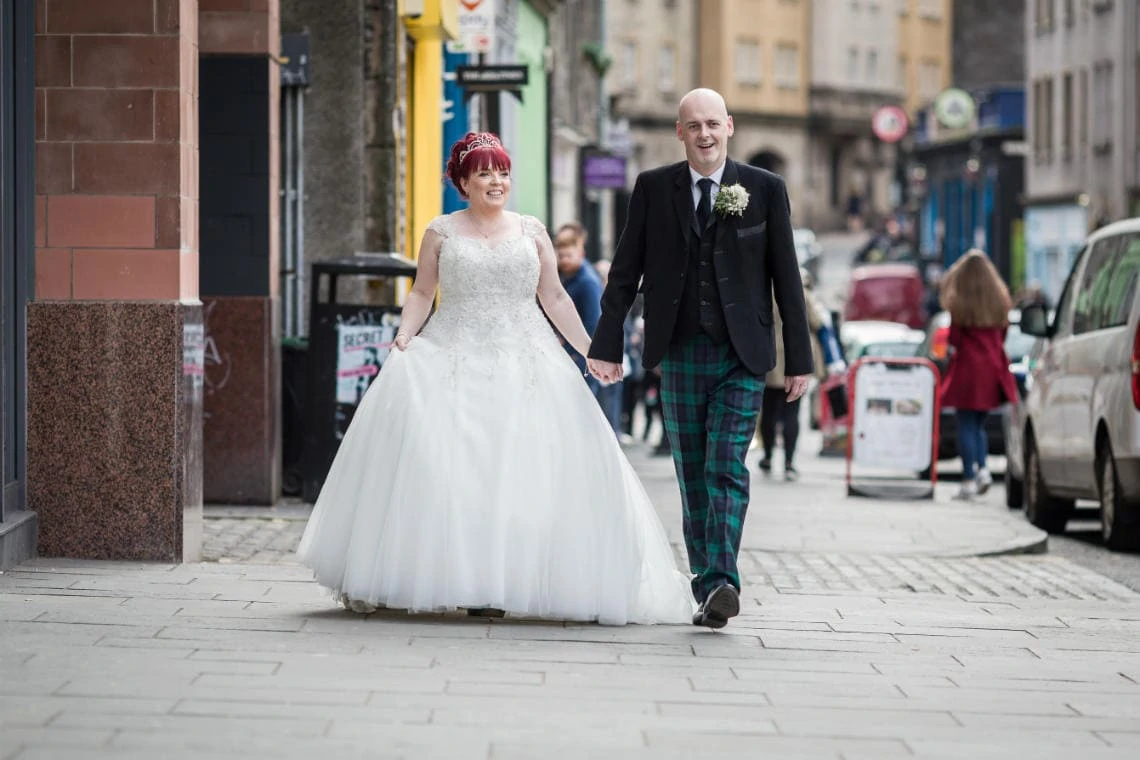 bride and groom walking hand in hand through Grassmarket
