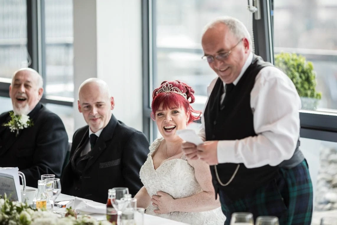 bride with wedding party laughing during father of bride speech