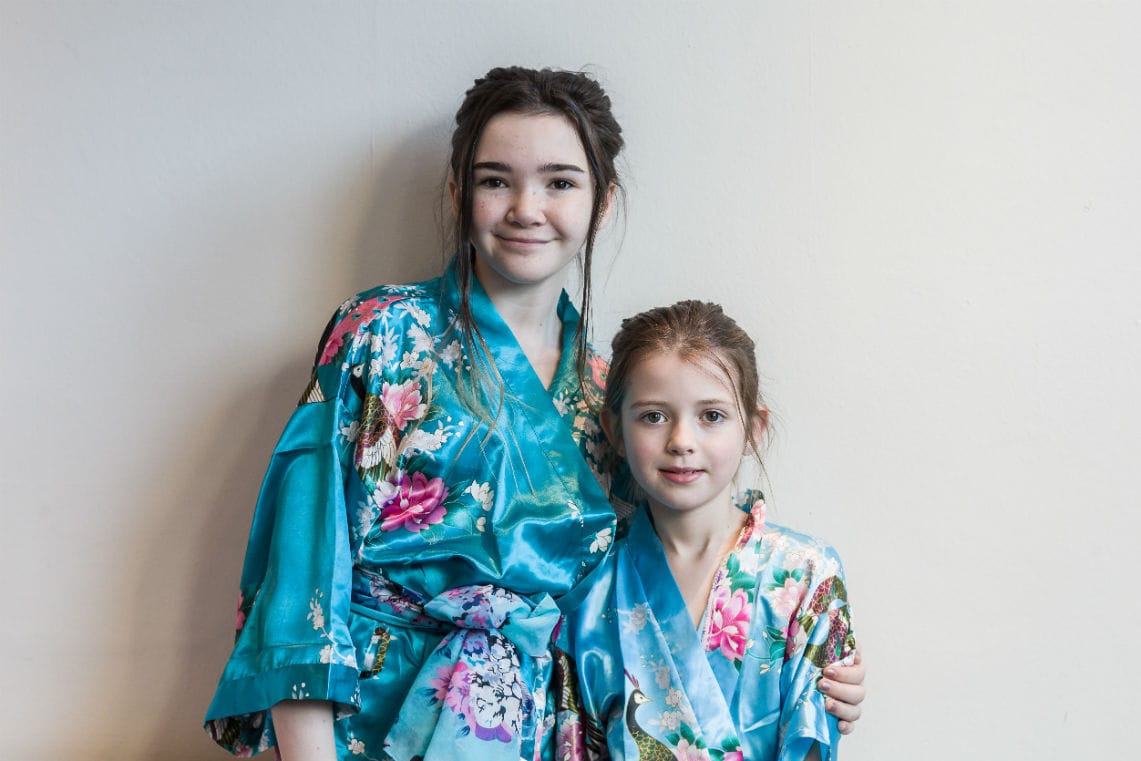 two young girls wearing matching blue silk robes smiling at camera