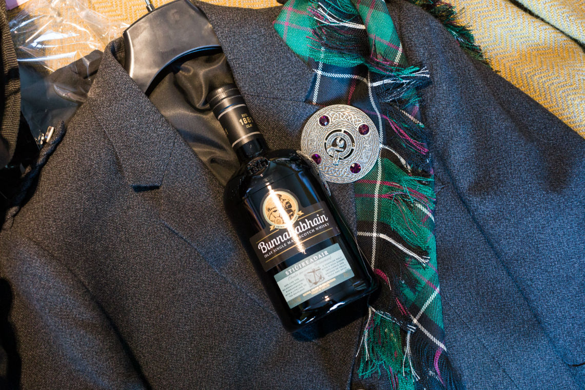 bottle of whisky laying on suit jacket and tartan plaid