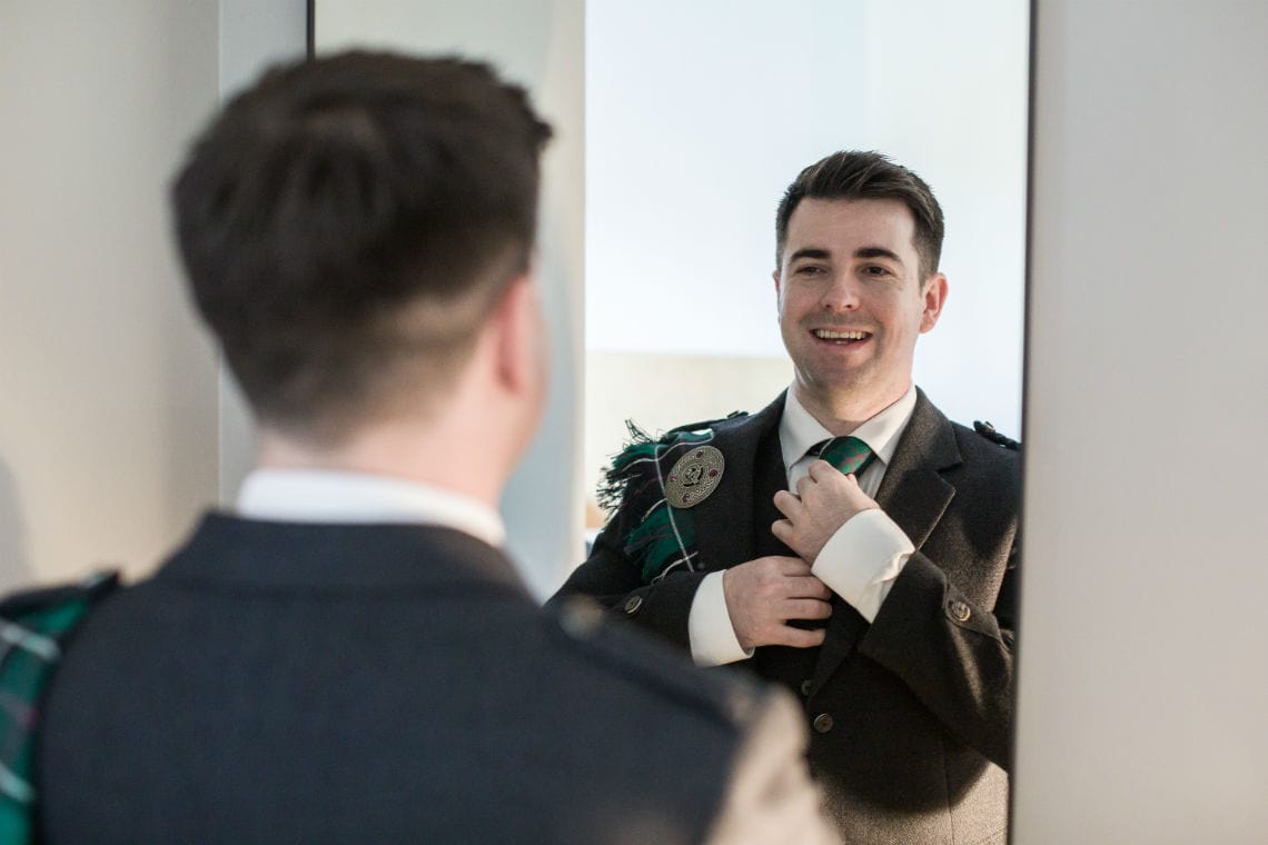 groom looking into mirror and smiling as he adjusts tie