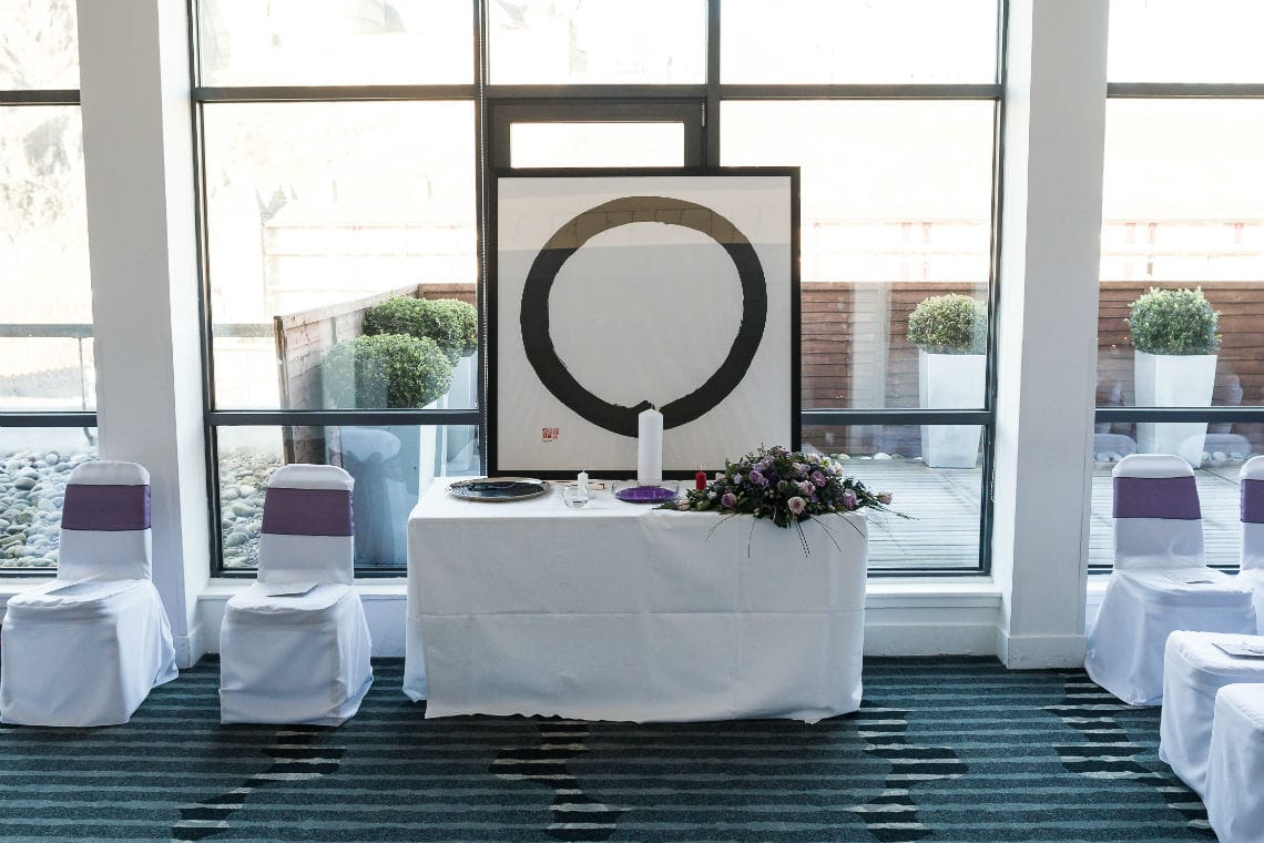 Framed picture of Buddhist Enzo symbol sitting on table with white tablecloth in hotel ceremony room