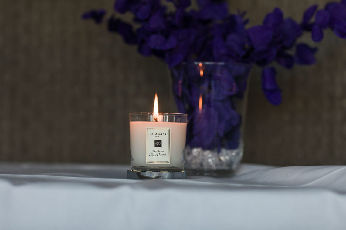 lit Jo Malone candle beside vase of purple flowers sitting on table