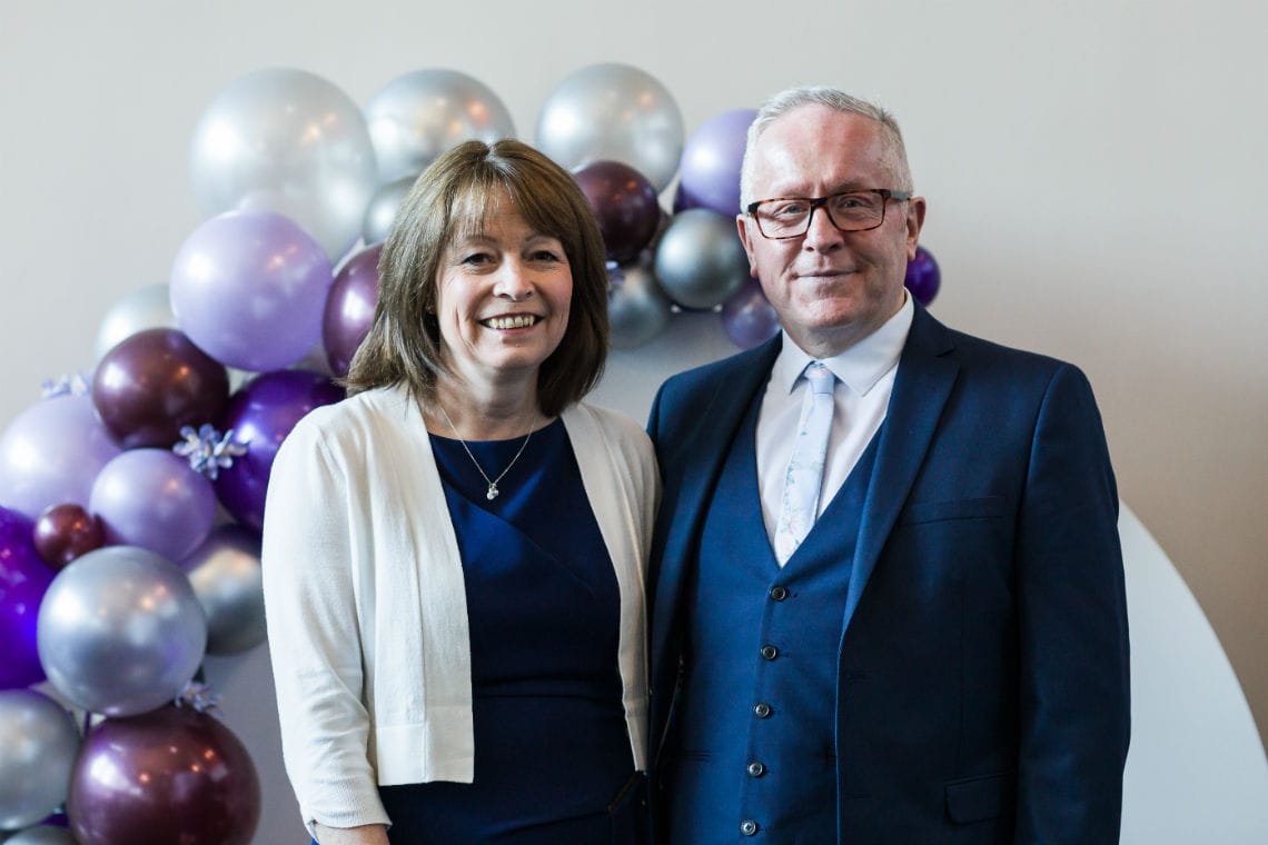 portrait of couple standing in front of silver and purple balloon arch