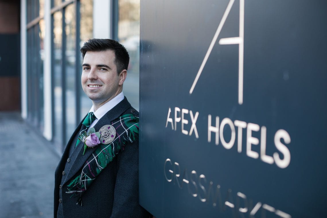portrait of groom in front of hotel sign