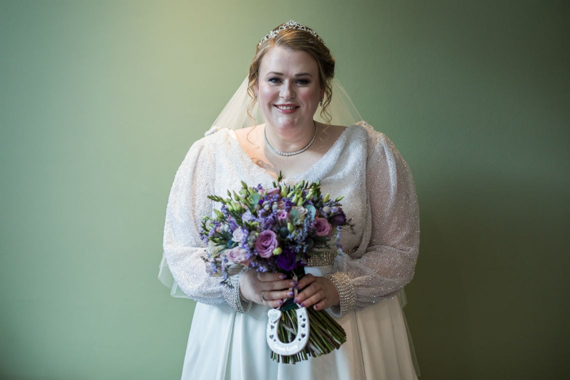 portrait of bride standing up wearing her wedding gown and holding her bridal bouquet