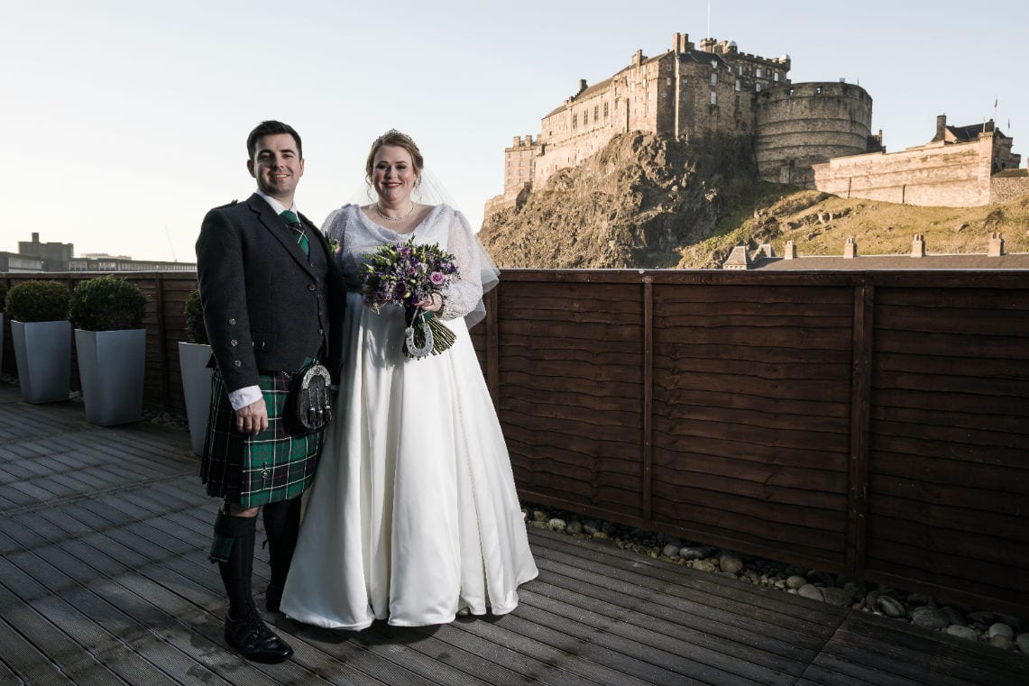 newlywed photo of bride and groom on rooftop terrace with Edinburgh Castle in the backdrop