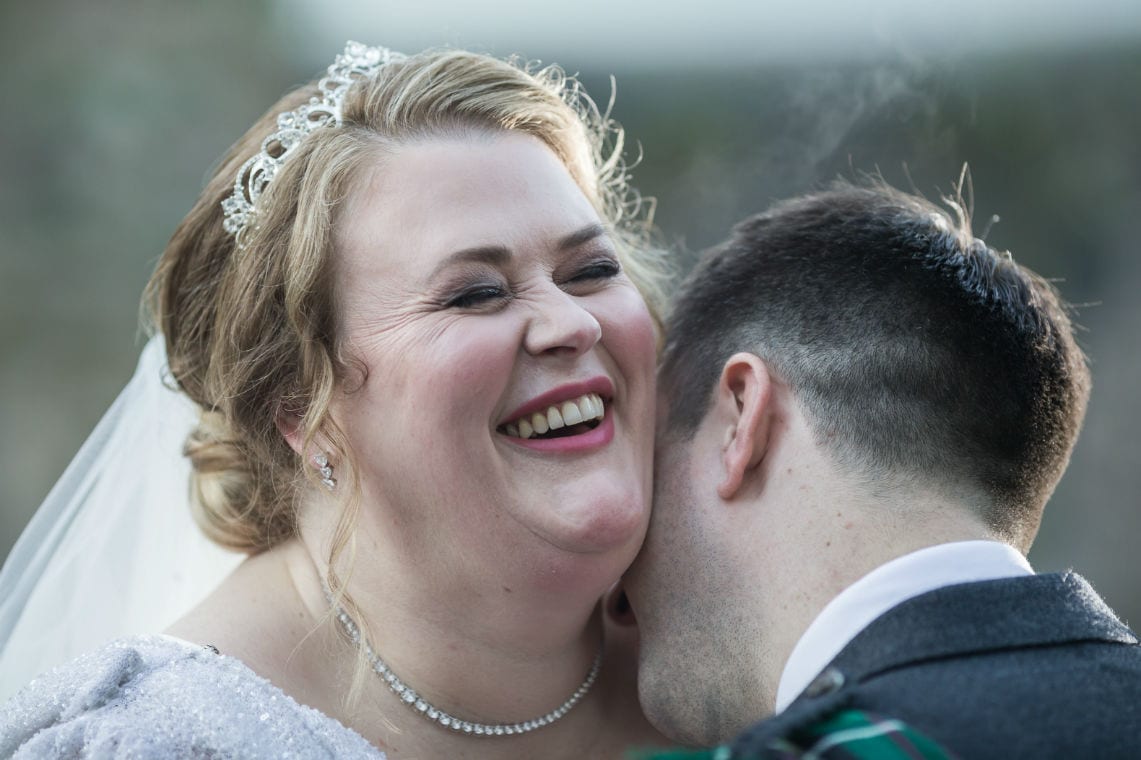 bride laughing as groom kisses her neck