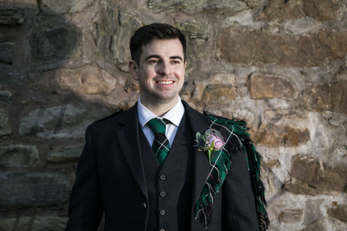 portrait of groom smiling in front of brick wall on newlywed photoshoot
