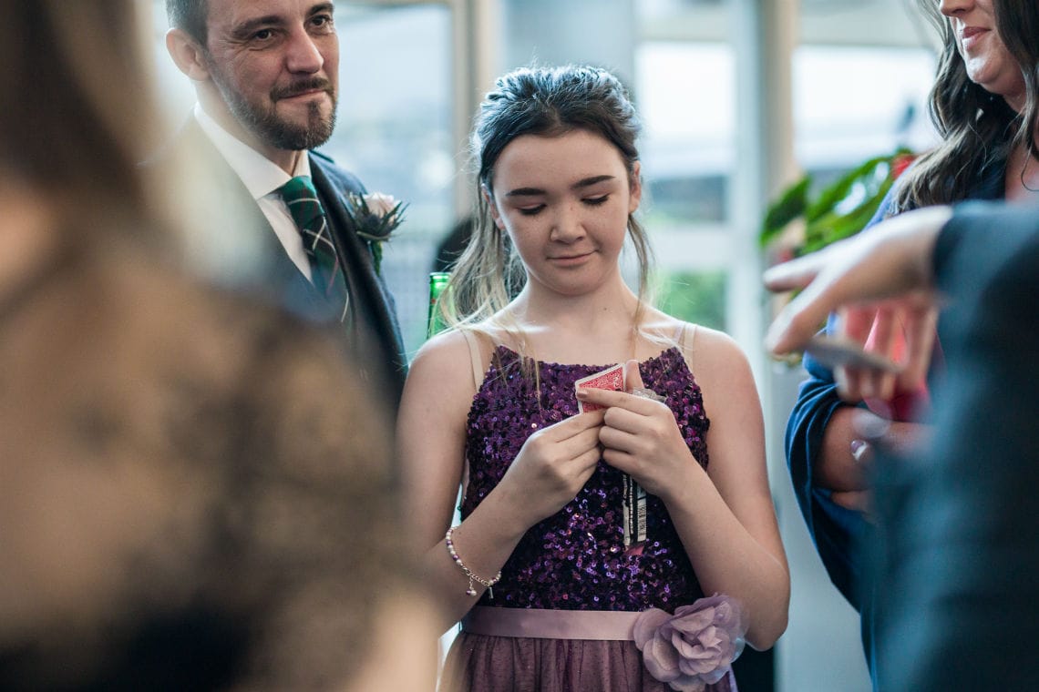 young girl checking her playing card during a magic trick at the reception