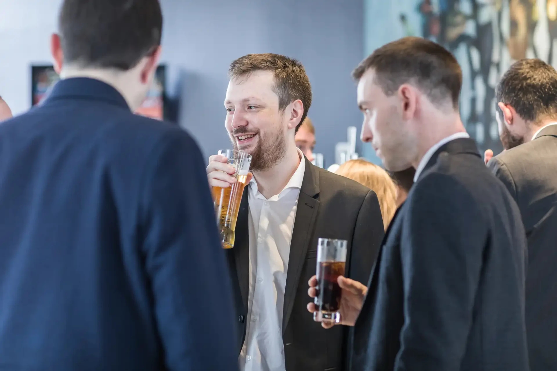 A group of men in business attire, socializing at a networking event with drinks in their hands.