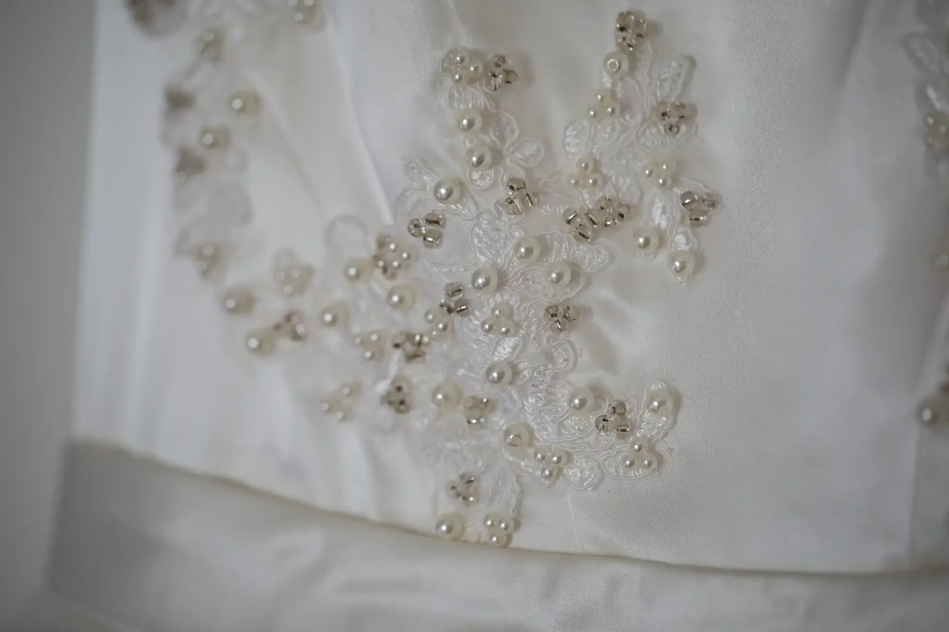 Close-up of a white wedding dress with detailed pearl and bead embroidery on lace applique.