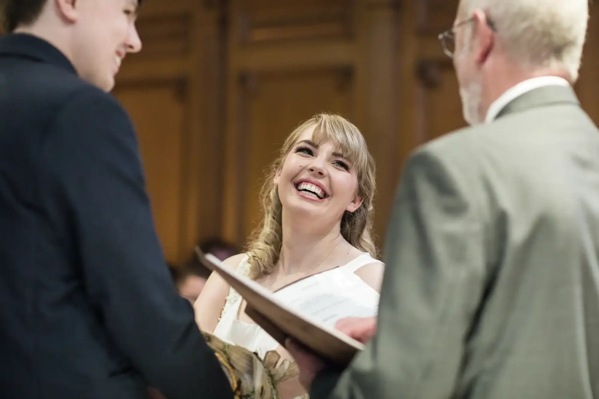 A young woman with a joyful expression receives a certificate from an older man as another man watches in a formal indoor setting.