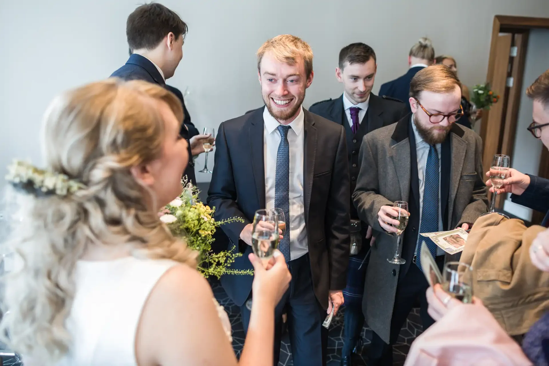 A bride conversing with a group of smiling men holding drinks at a wedding reception.