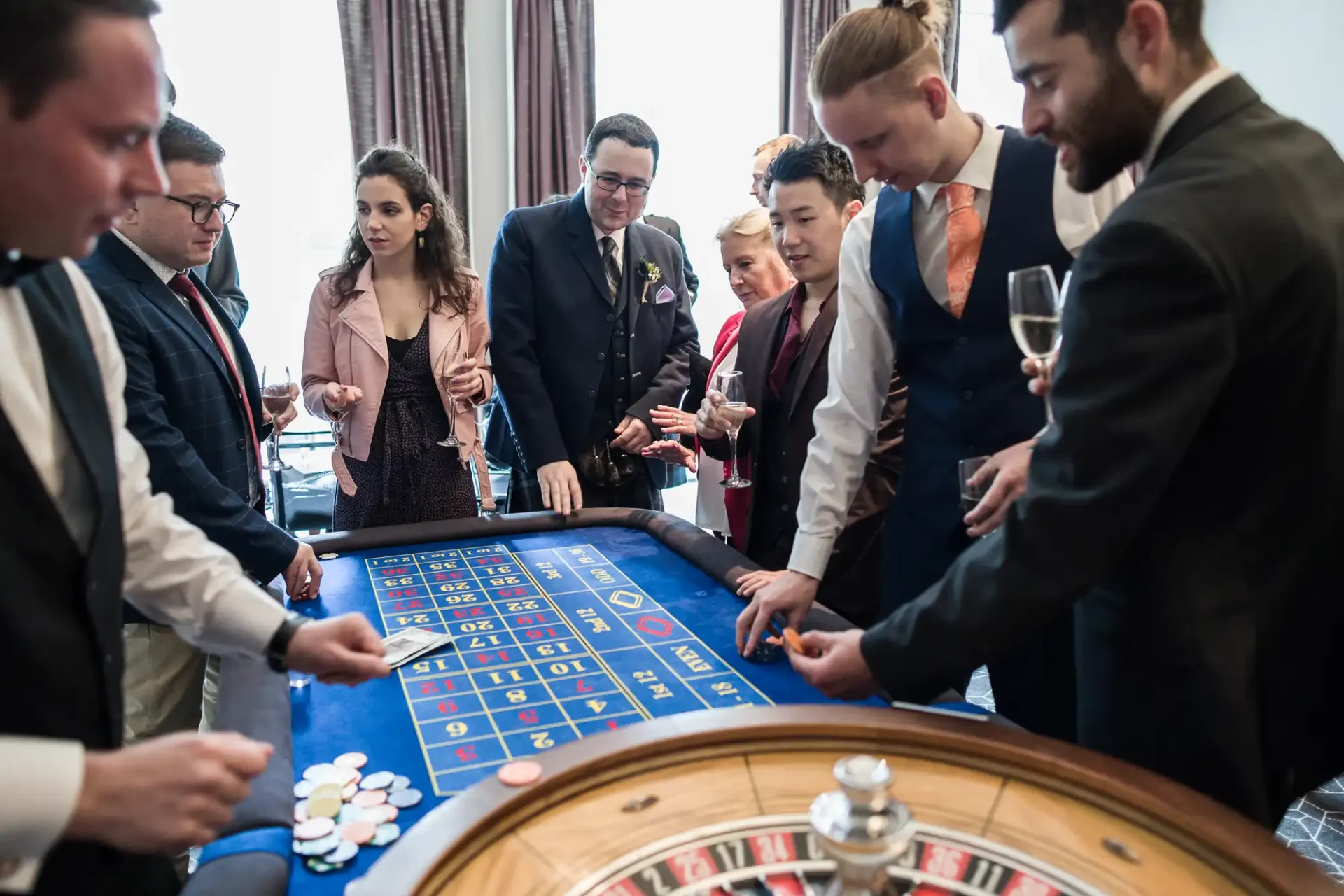 Group of people standing around a roulette table at a casino, engaged in placing bets with chips.