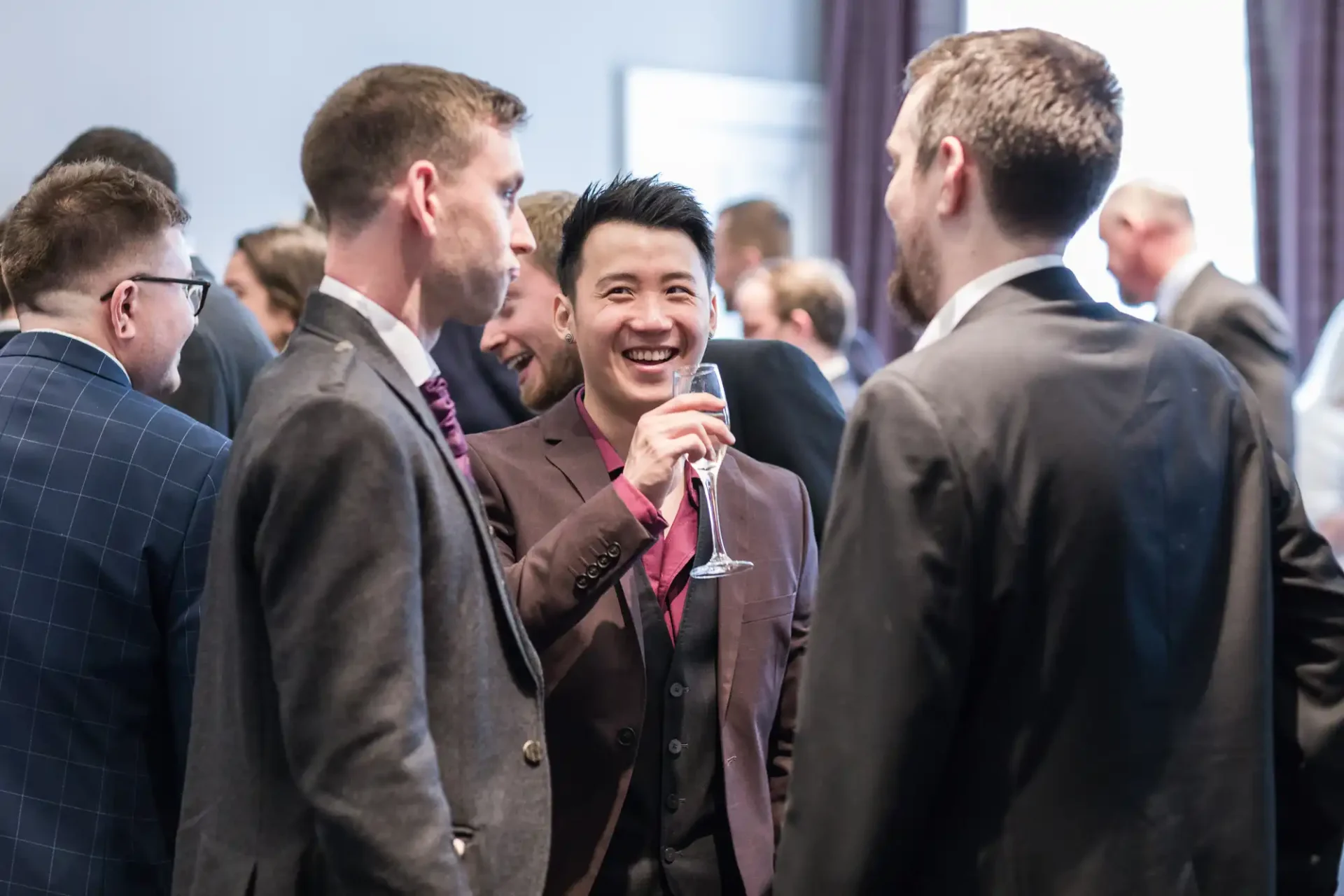 Group of men in formal attire engaging in conversation at a networking event, with one man smiling and holding a drink.