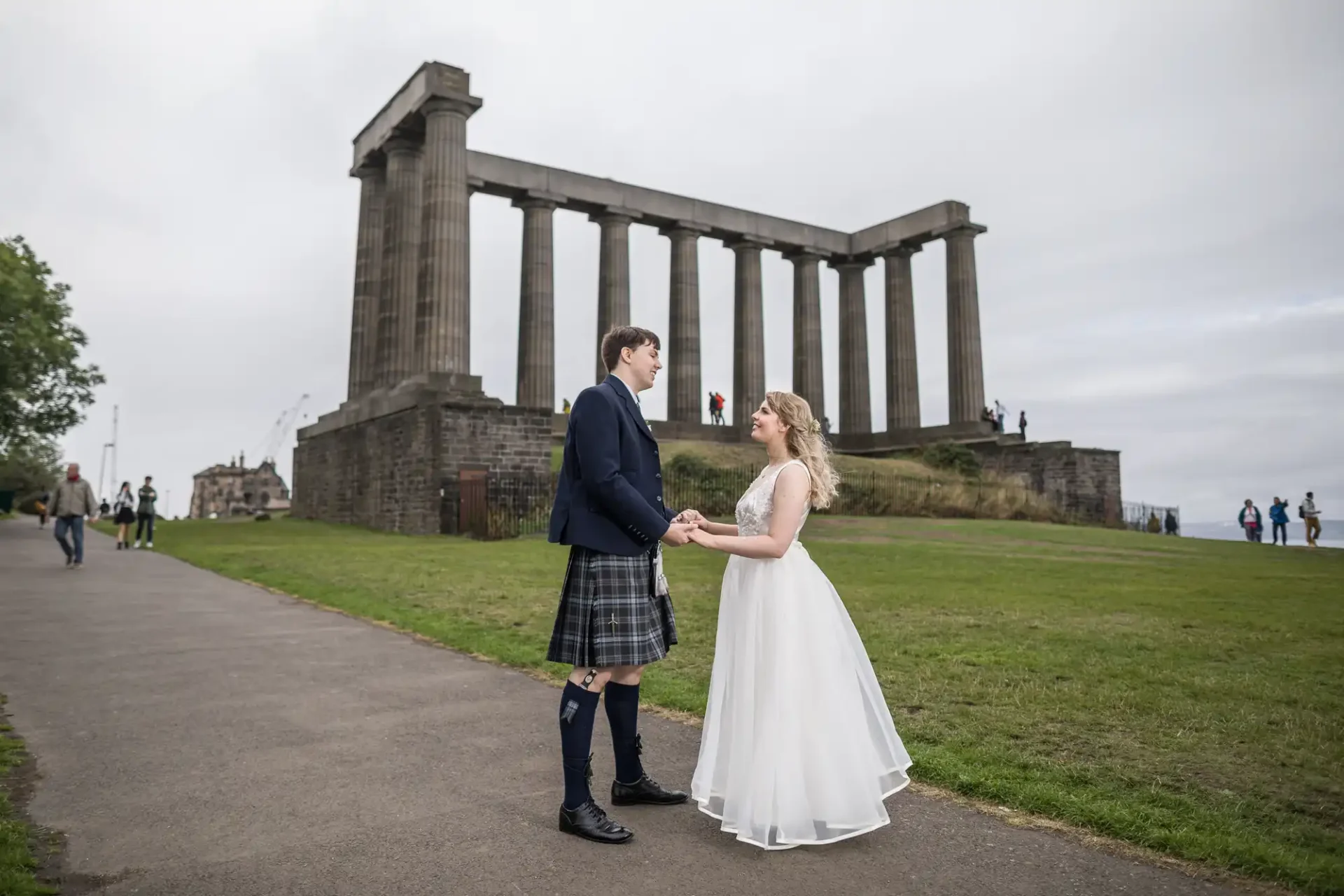 A bride and groom holding hands at calton hill in edinburgh, with the national monument in the background.