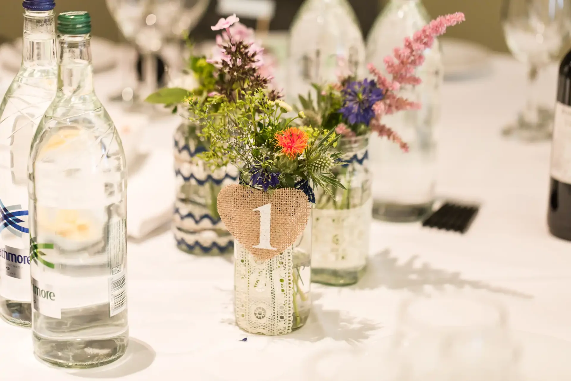 Elegant table setting featuring a floral centerpiece in a decorated vase marked with the number "1," accompanied by two bottles of water.