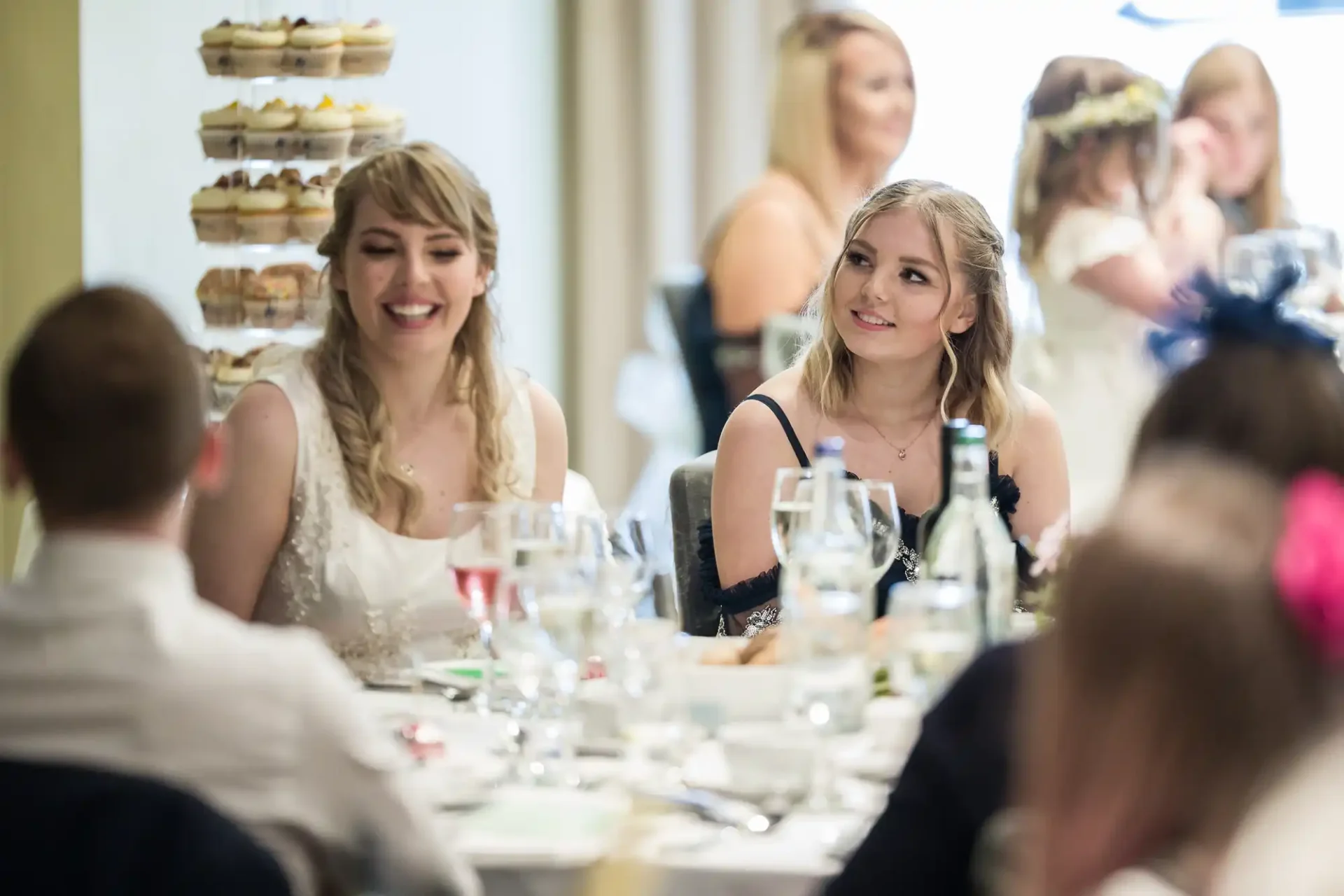 Two women smiling and interacting at a wedding reception table adorned with desserts and drinks.