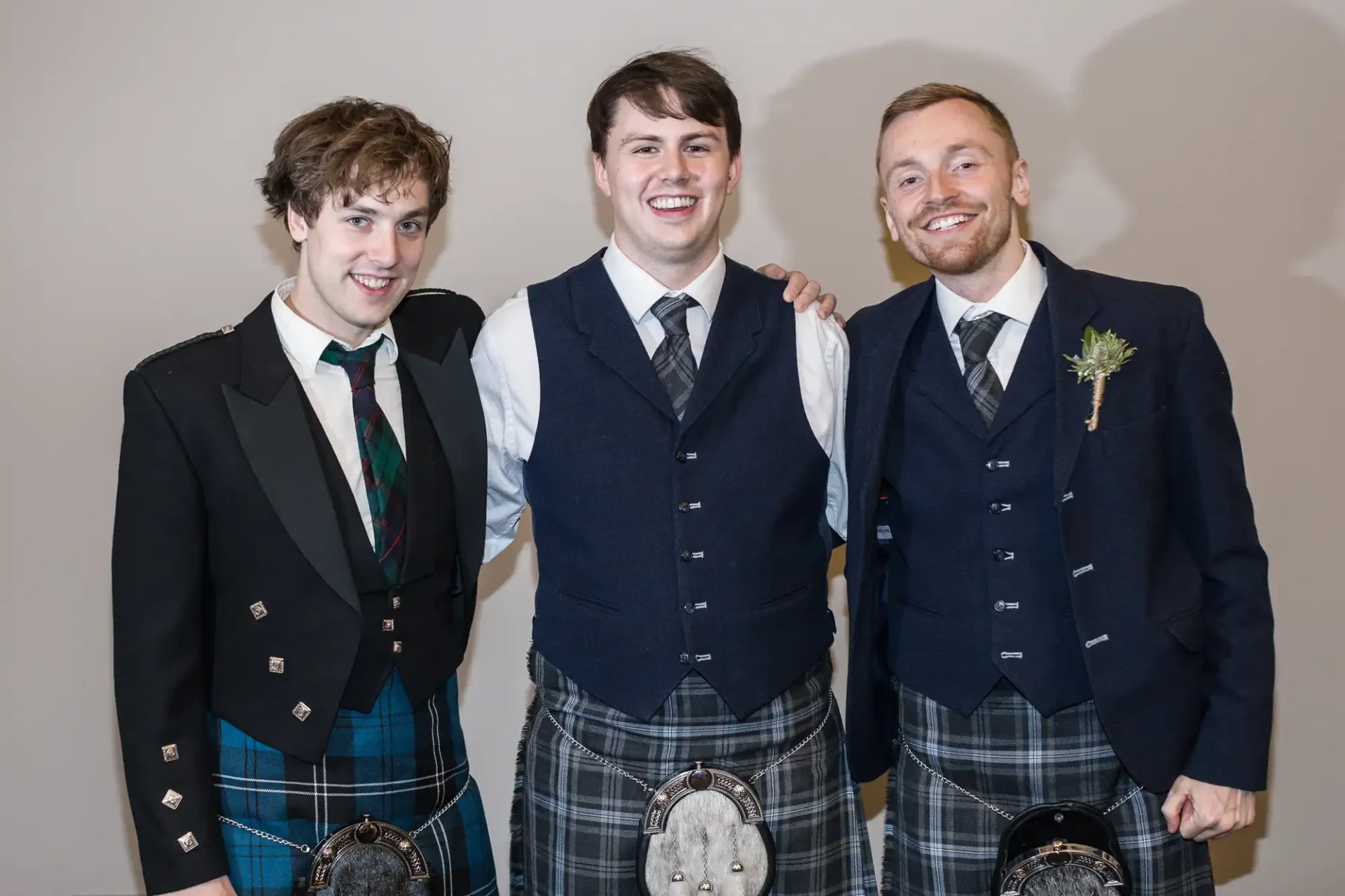 Three men in traditional scottish attire with kilts and waistcoats, smiling at a formal event.