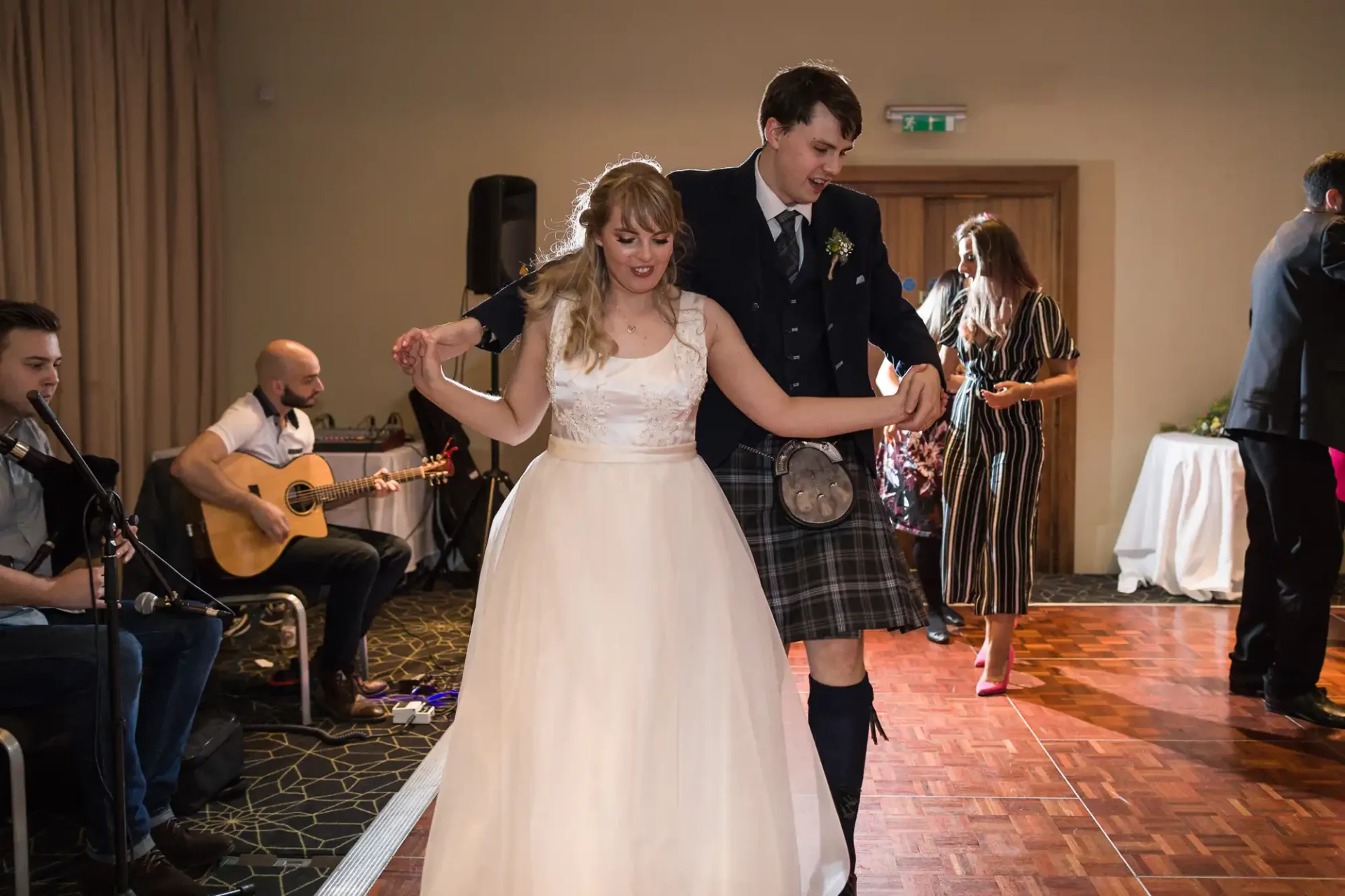 A bride and groom joyfully dance together in a ballroom, with a live band playing in the background.