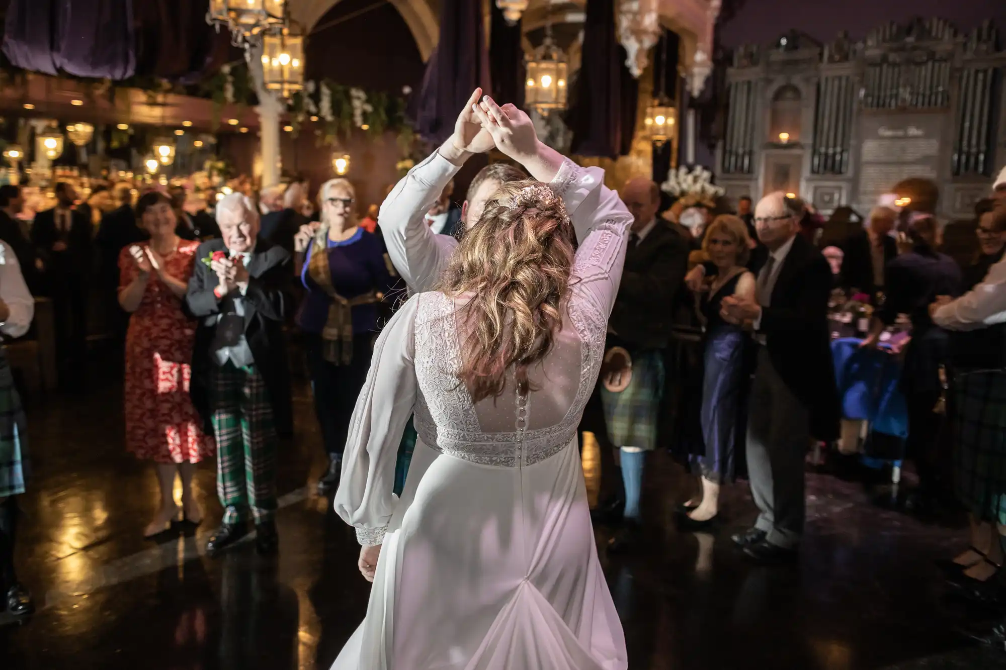 A couple dances in the center of a crowd at a formal event with dim lighting and elegant decor.