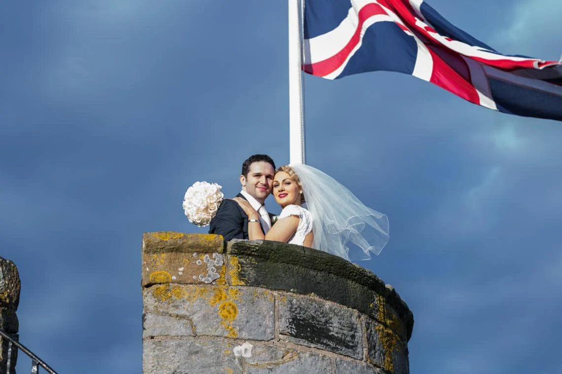 Auld Keep rooftop turret newlyweds embrace below the Union Jack