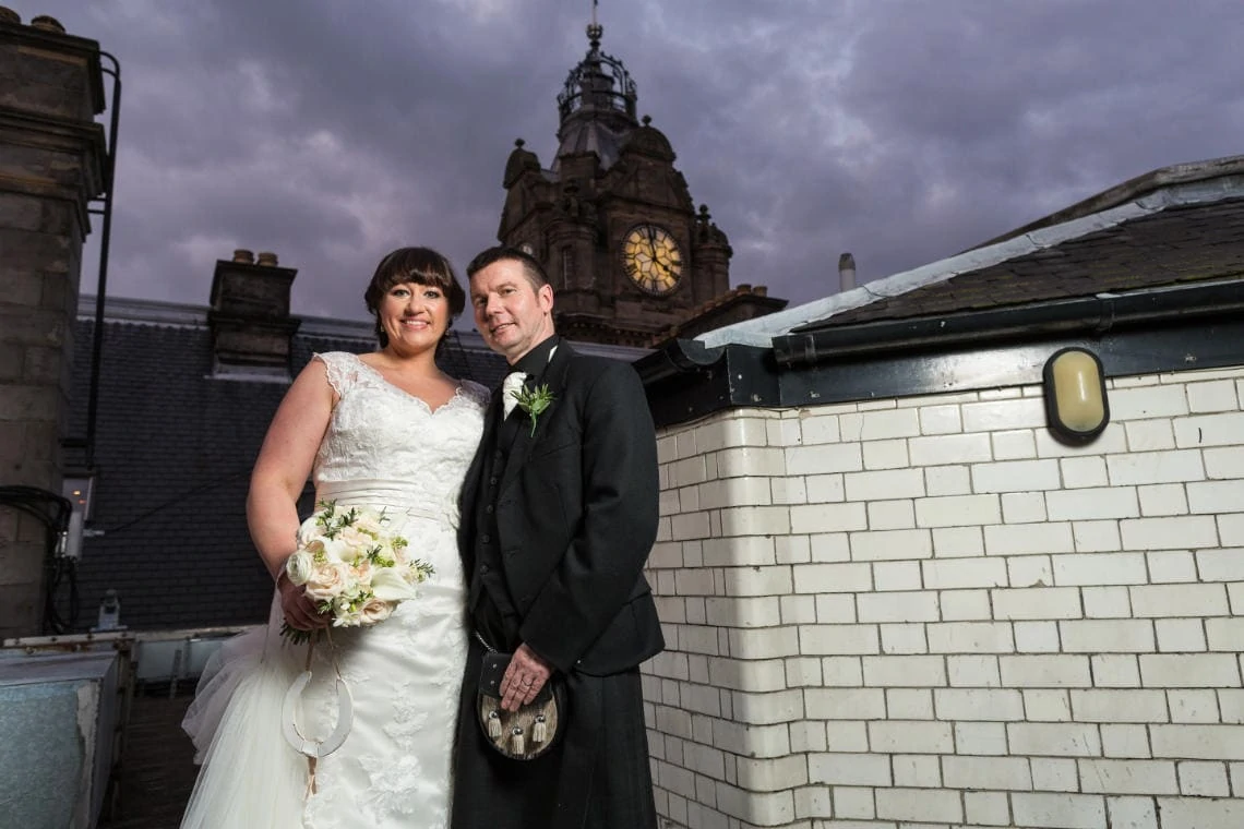 newlyweds on the roof of the Balmoral Hotel at dusk with the clock tower in the background