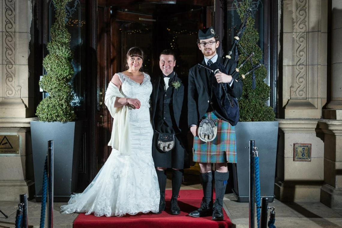 newlyweds with the piper at the entrance to the Balmoral Hotel