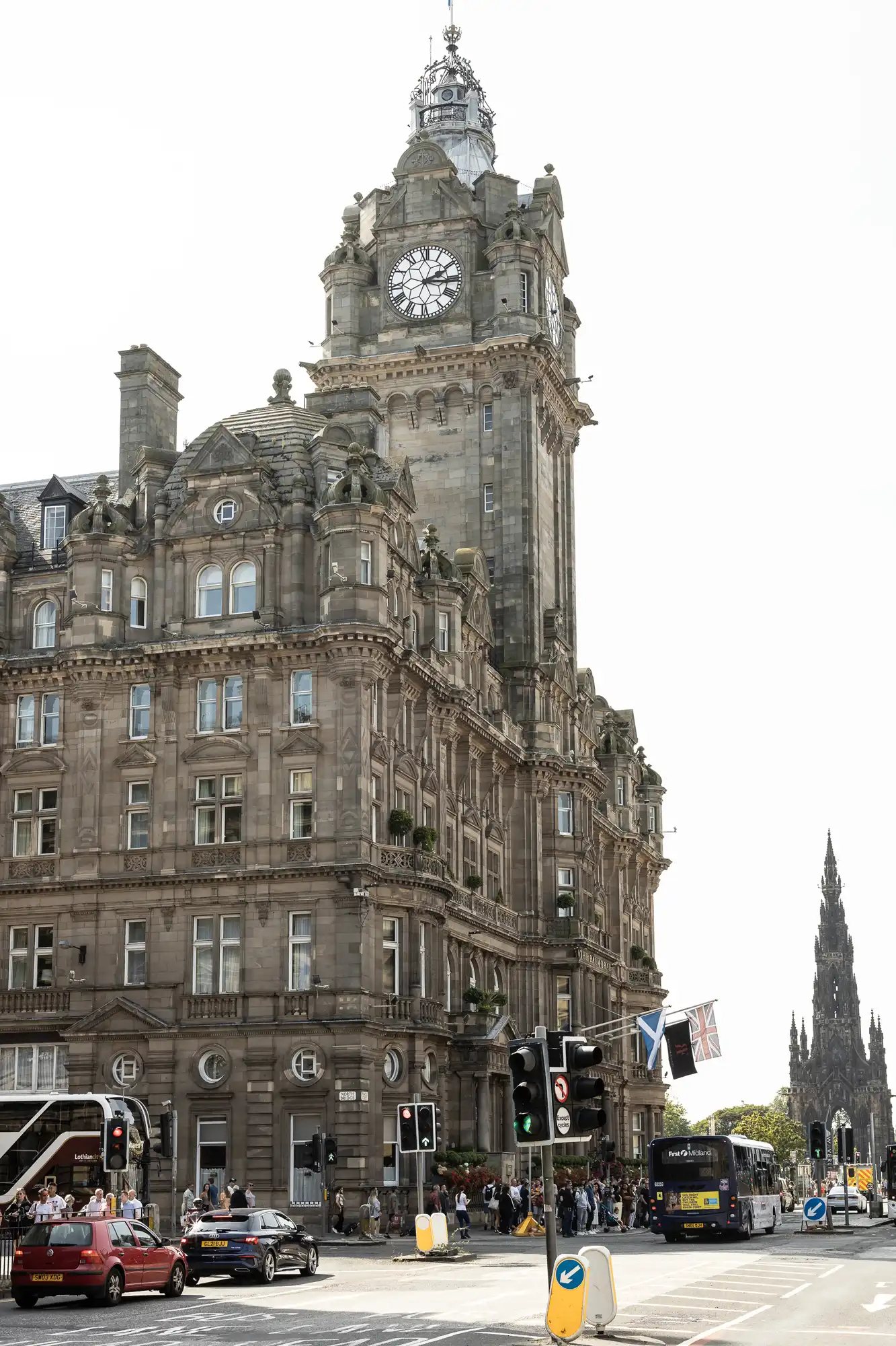 A bustling street scene at the base of the balmoral hotel in edinburgh, featuring the hotel's grand clock tower, vehicles, and pedestrians.