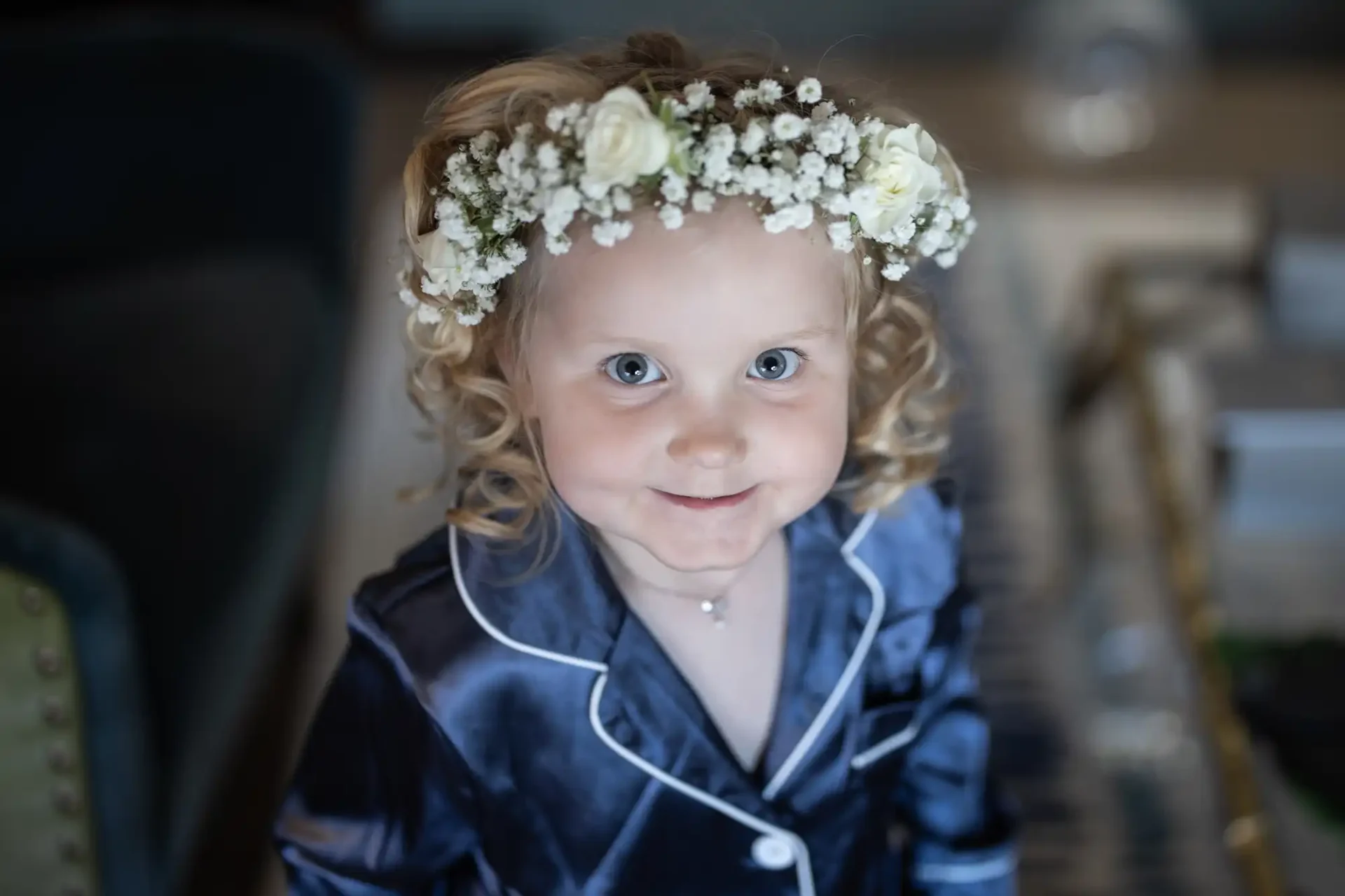 A young child with curly hair wearing a floral headband and a blue satin outfit, smiling at the camera.